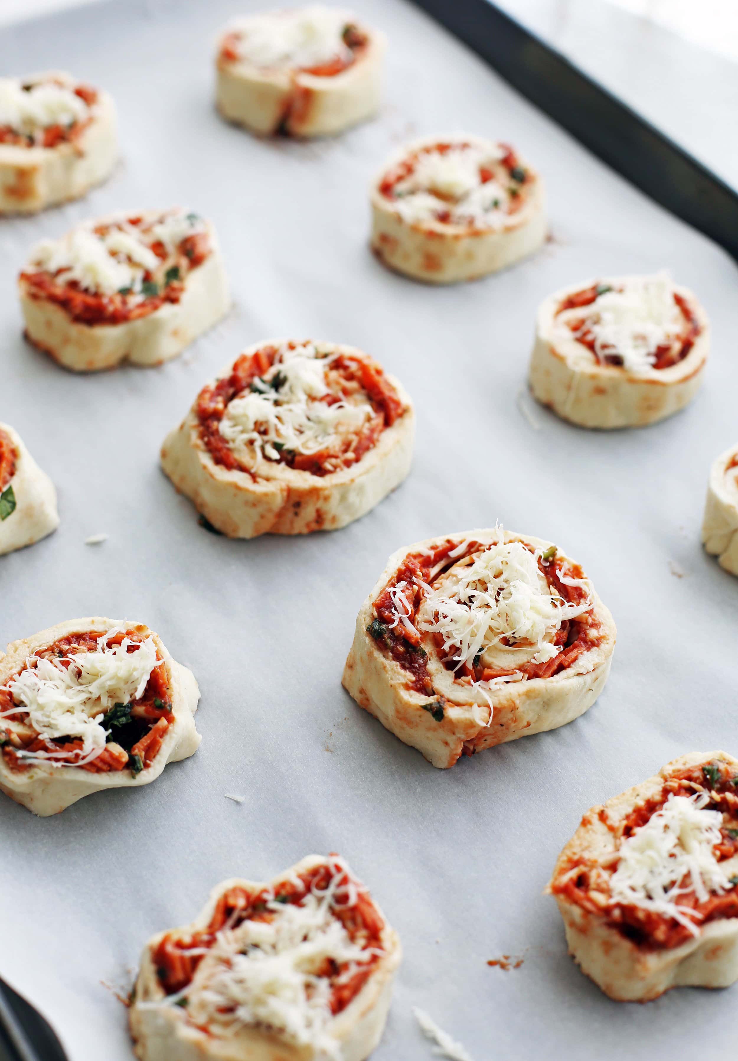 Unbaked pepperoni cheese pizza rolls on a parchment paper lined baking sheet.