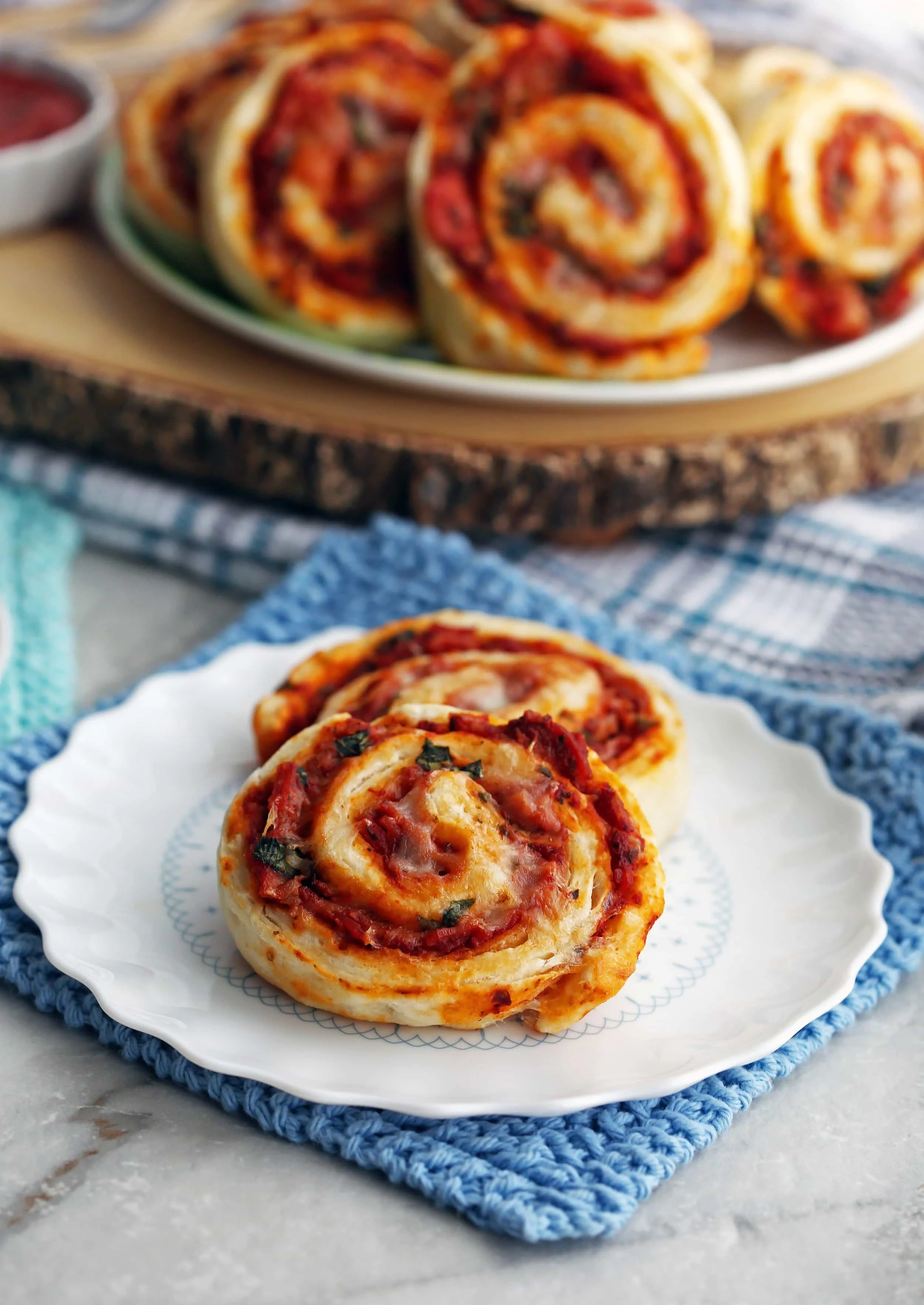 Two pepperoni cheese pizza rolls on a white plate with more pizza rolls on a plate behind them.