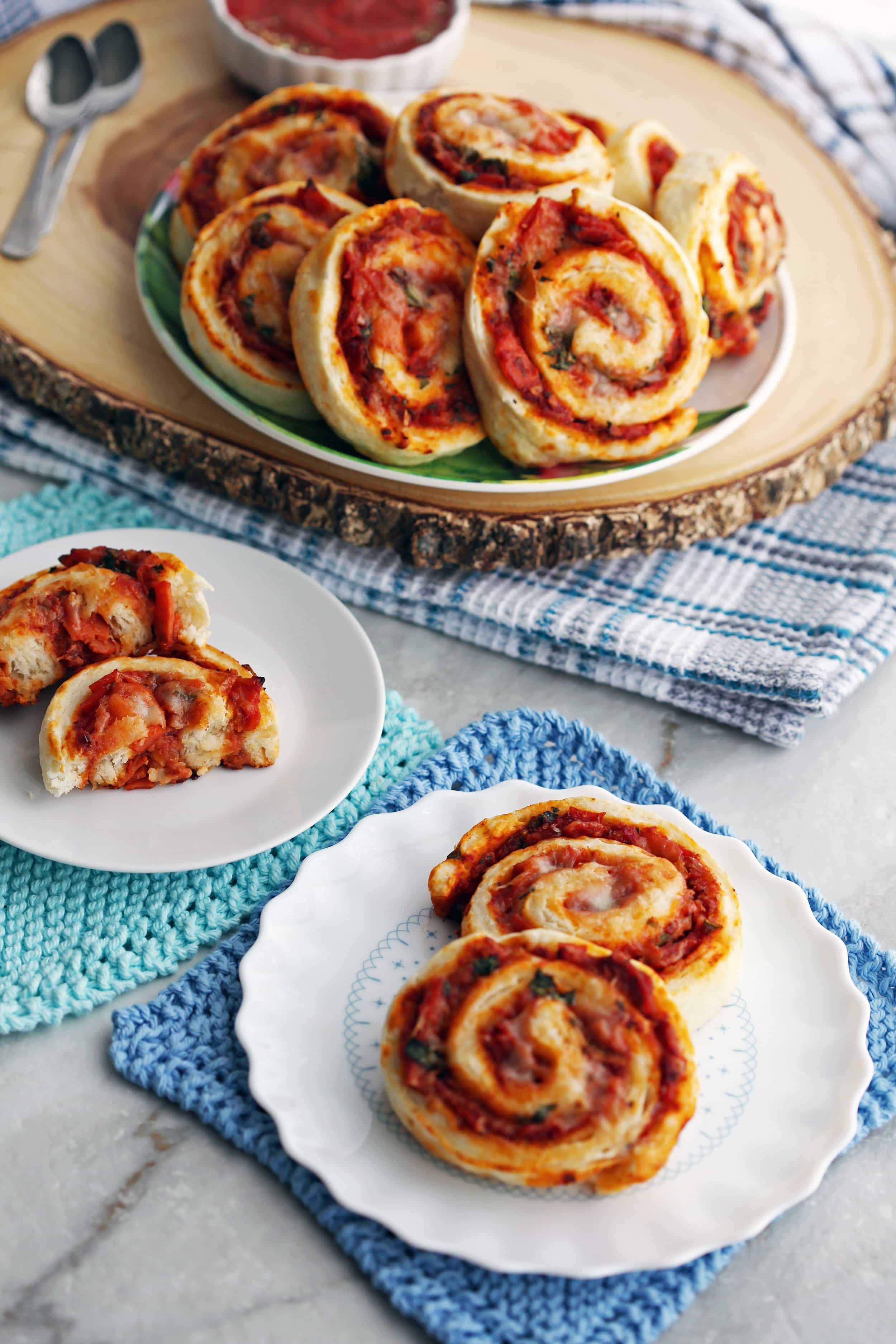 Three white plates containing many freshly baked pepperoni cheese pizza rolls.