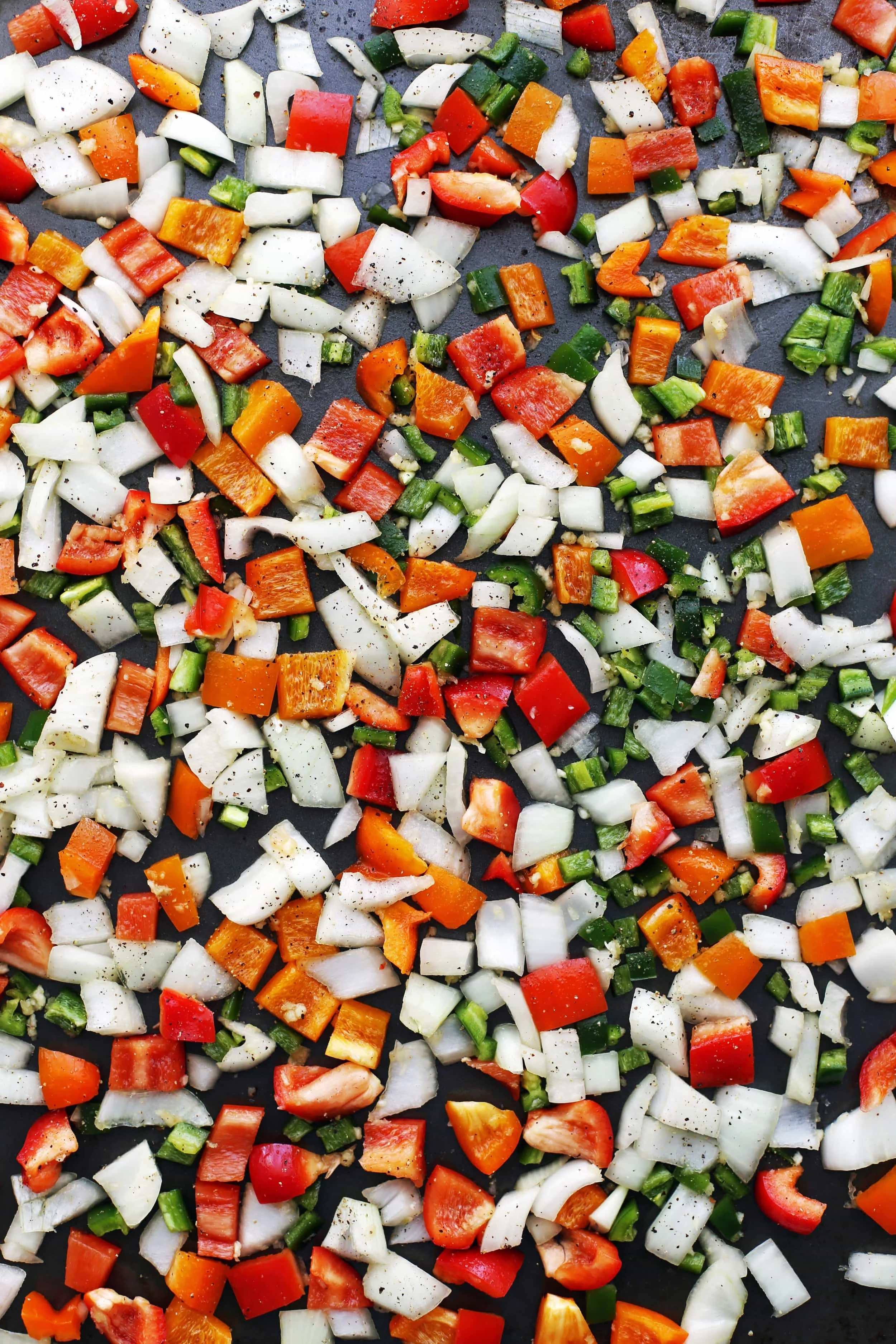 Chopped bell peppers, jalapenos, onions, and garlic on a baking sheet.