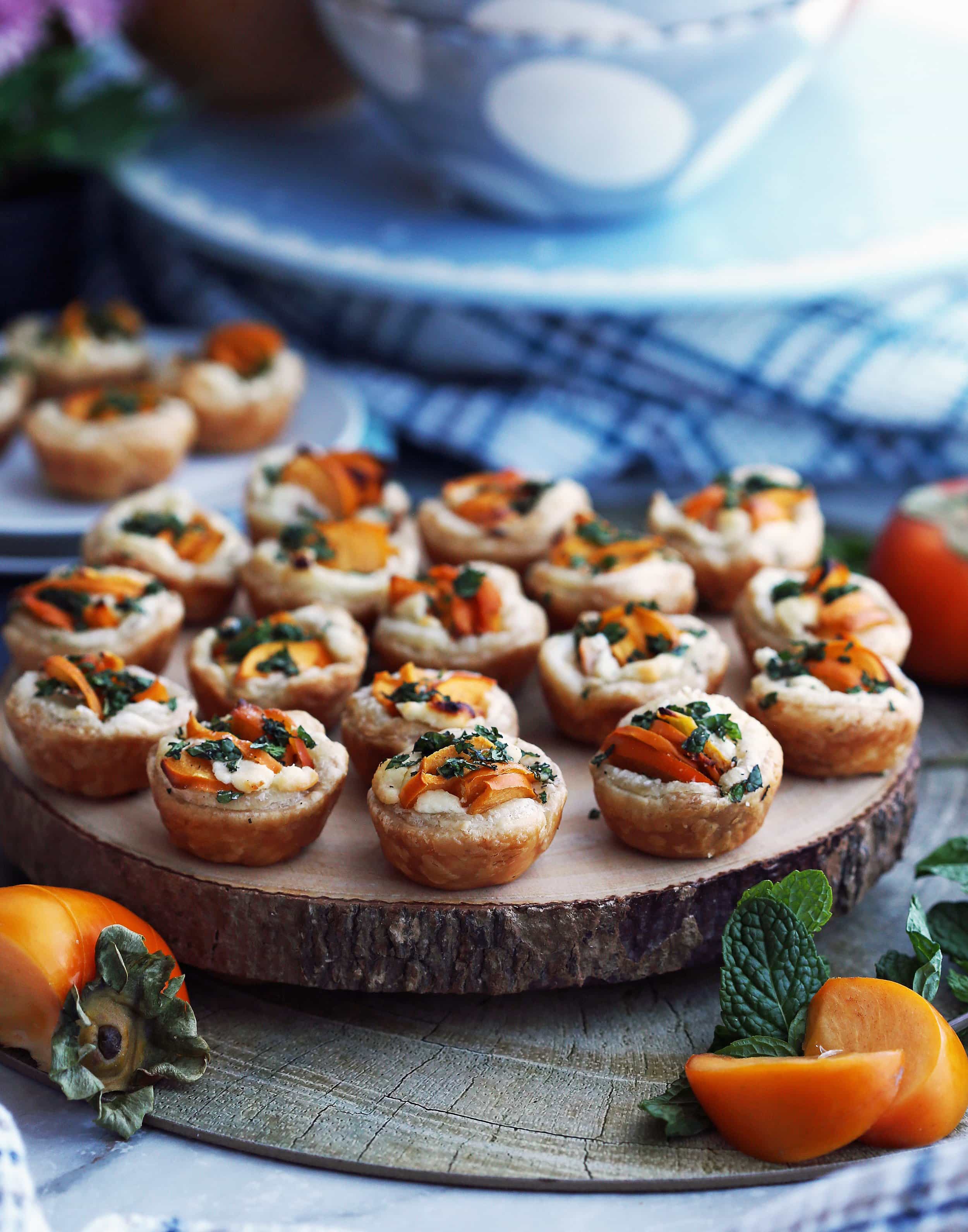 Over a dozen Persimmon Goat Cheese Tartlets garnished with fresh mint on a wooden platter.
