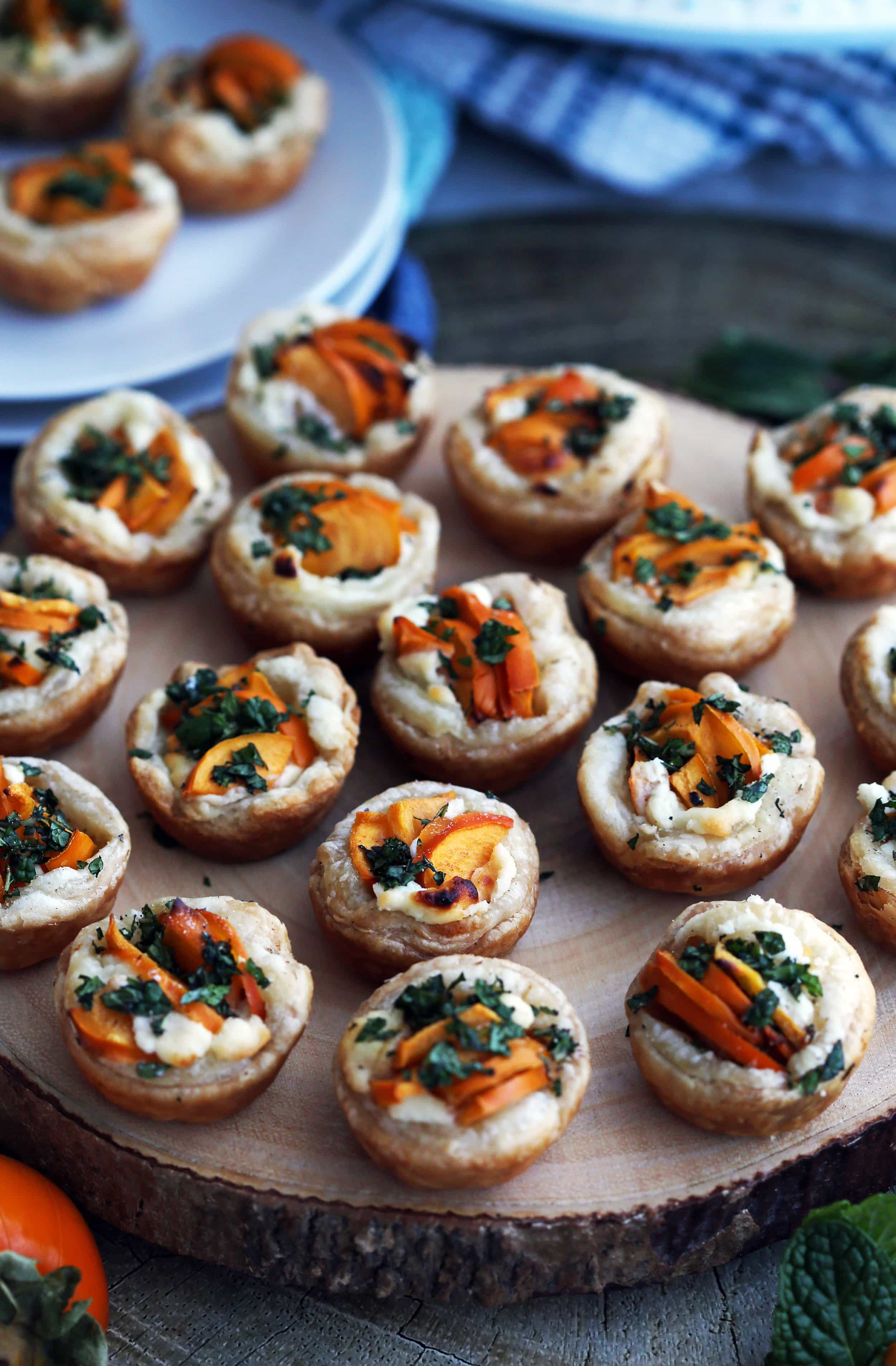 Persimmon Goat Cheese Tartlets with fresh mint topping on a large round wooden platter.