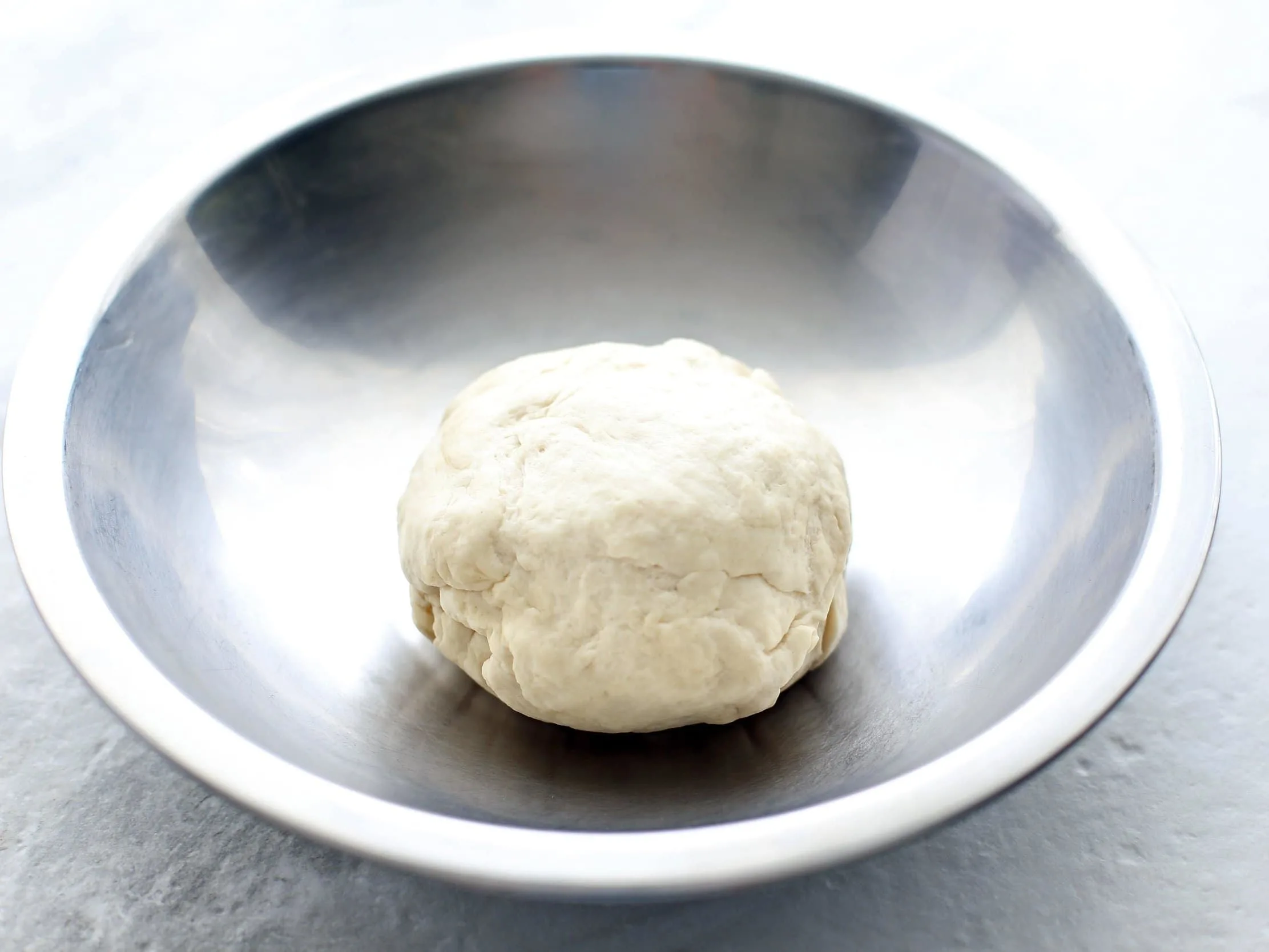 Pizza dough in a metal bowl.