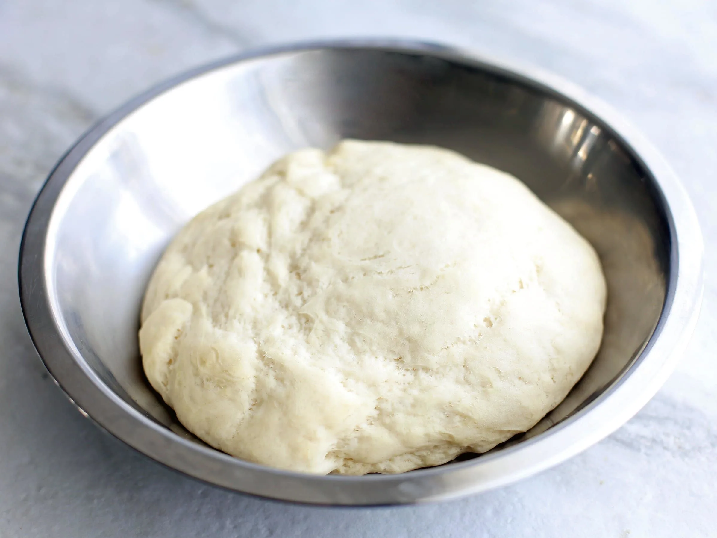 Proved pizza dough in a metal bowl.