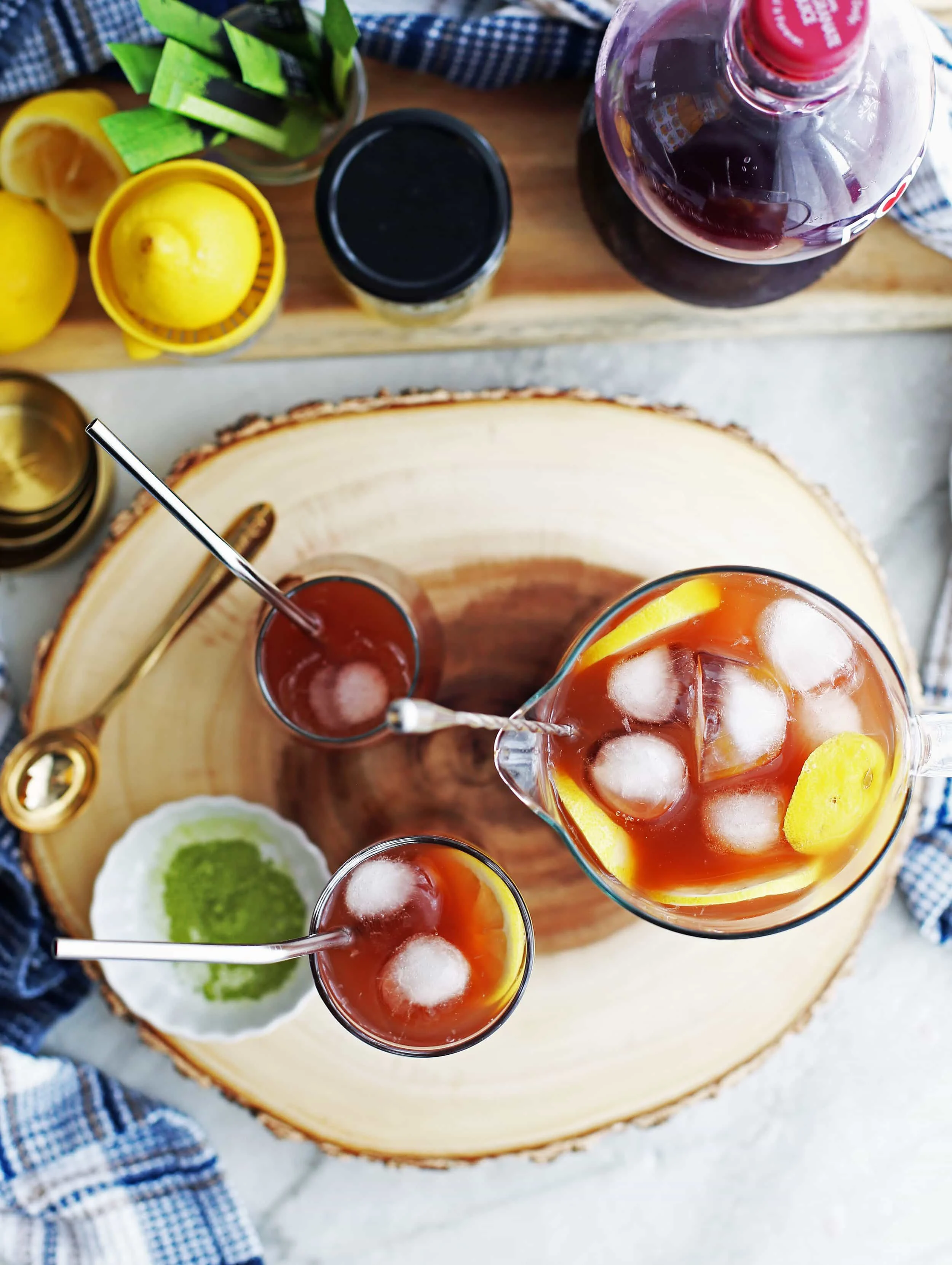 Overhead view of glasses and a pitcher full of pomegranate matcha iced tea with lemon slices and ice.