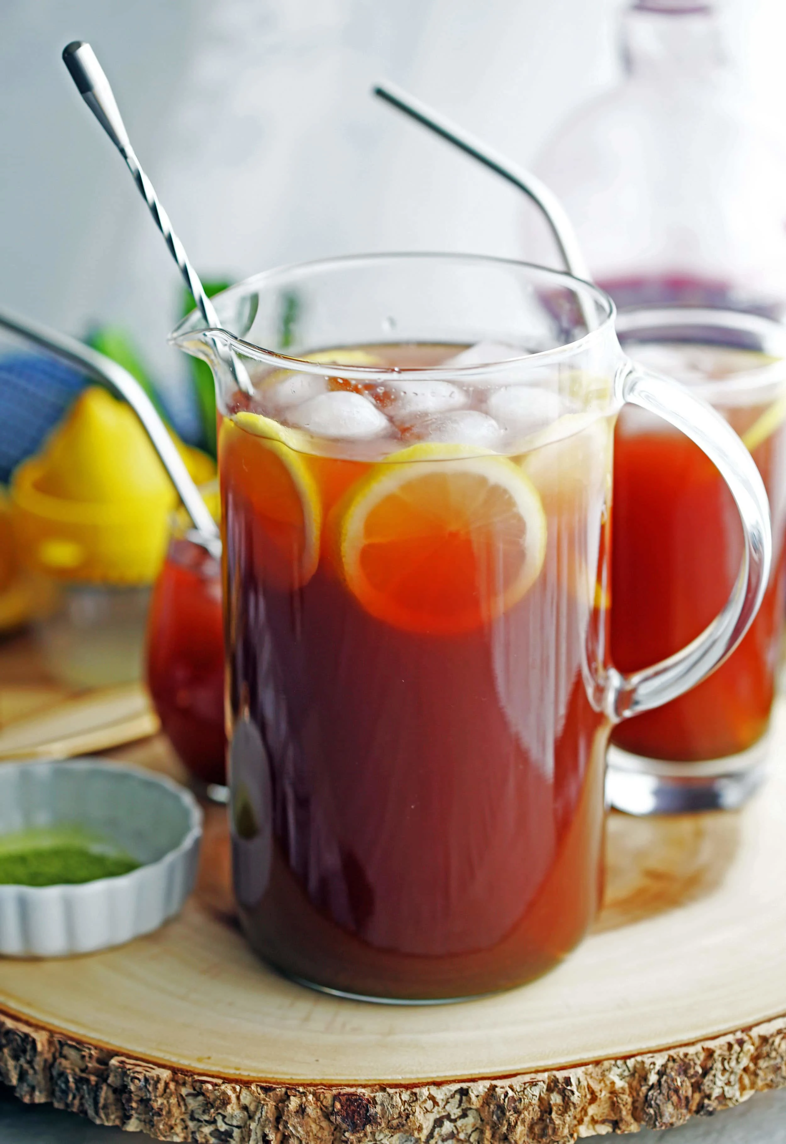 A large glass pitcher full of pomegranate matcha iced tea with lemon slices and ice.