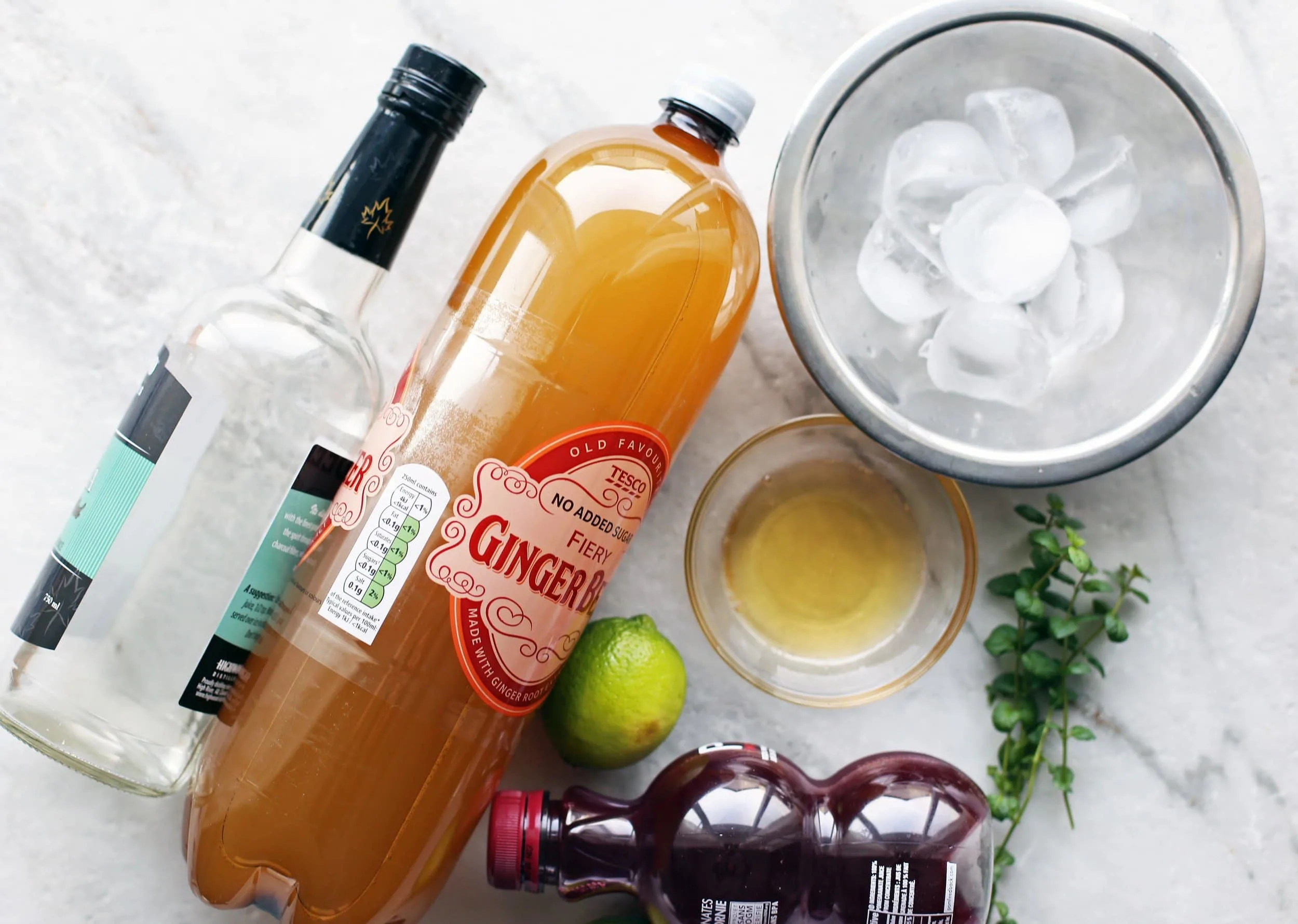 Overhead view of ginger beer, vodka, pomegranate juice, lime, honey, ice, and mint.