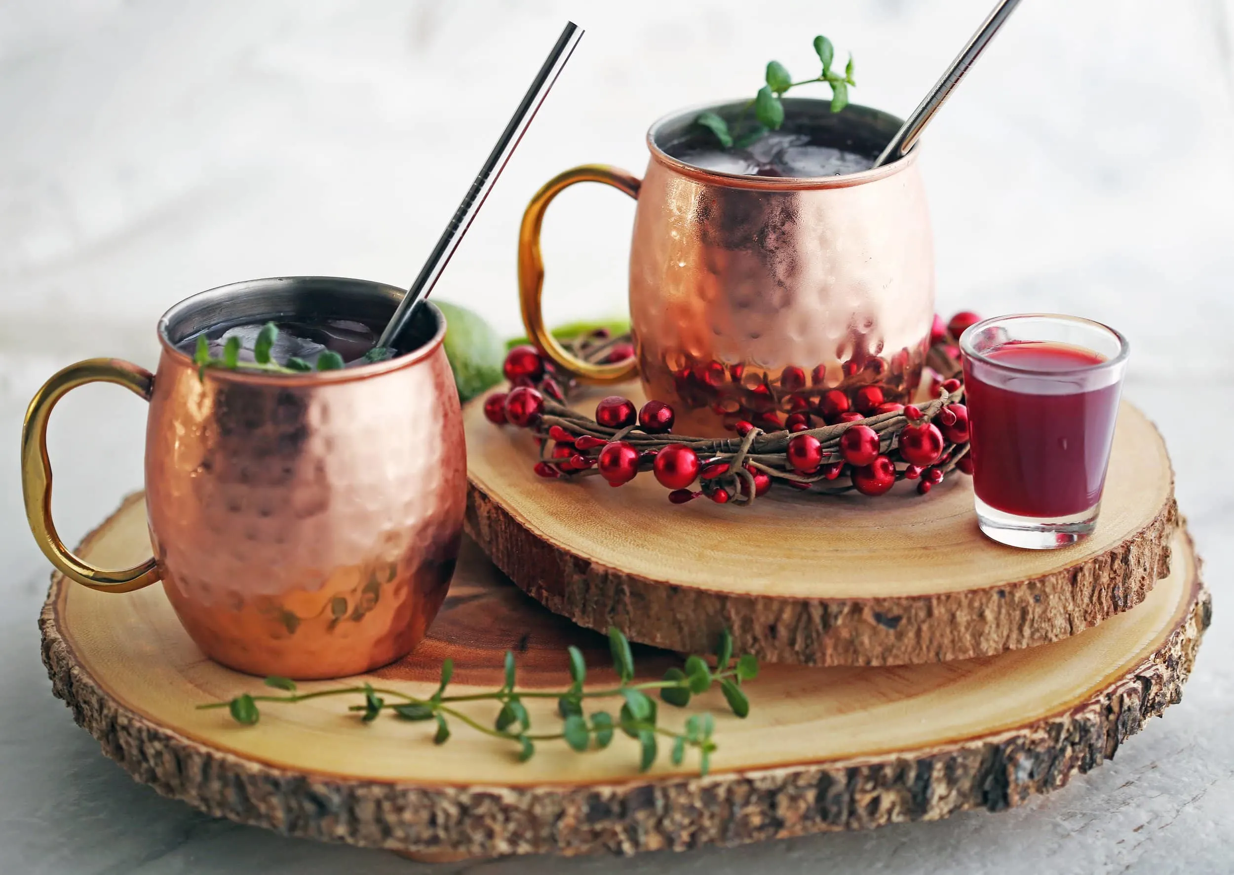 Two Pomegranate Honey Moscow Mule cocktails with mint garnish in copper mugs on two round wood slabs.