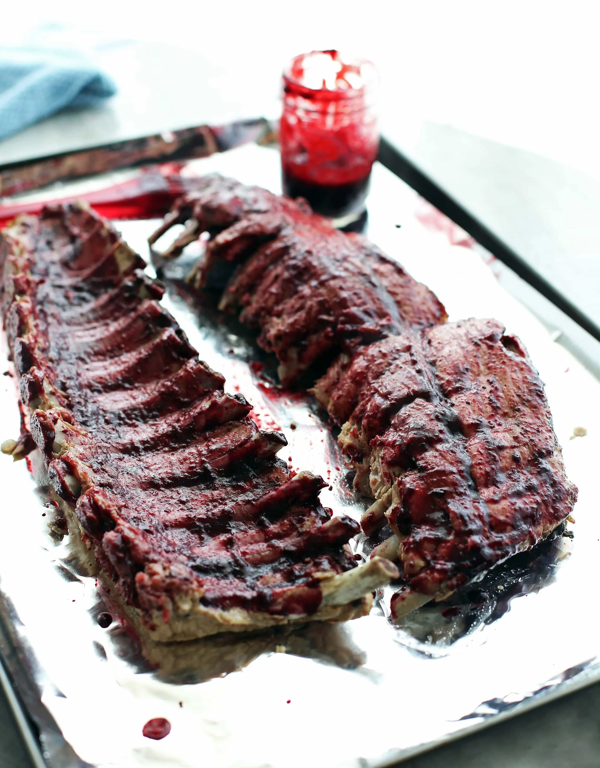 Two racks of baby back ribs covered with cherry chipotle sauce. on an aluminum-lined baking sheet.