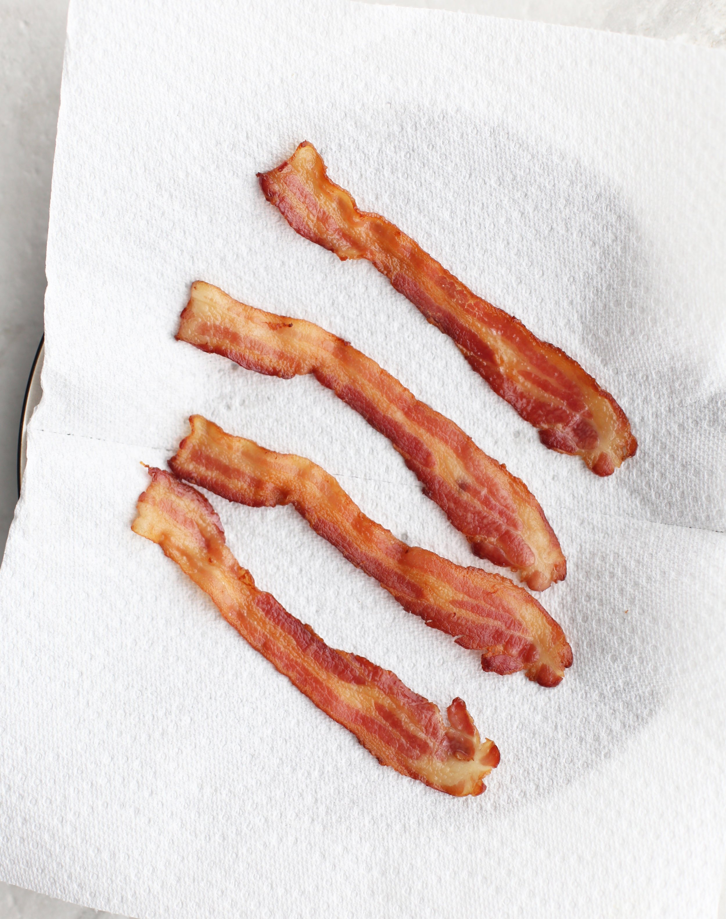 Four crispy strips of bacon on a white paper towel.