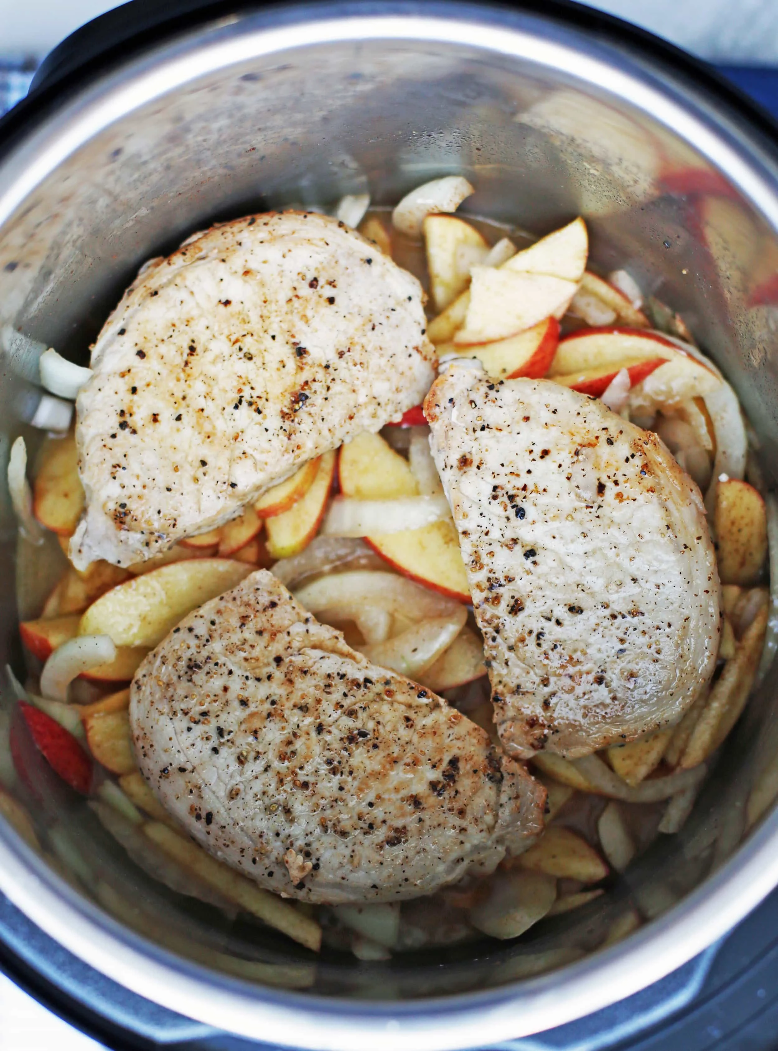 Sliced apples, sliced onions, ground cinnamon, lemon juice, salt, and chicken broth that’s topped with three browned boneless pork chops in an Instant Pot.