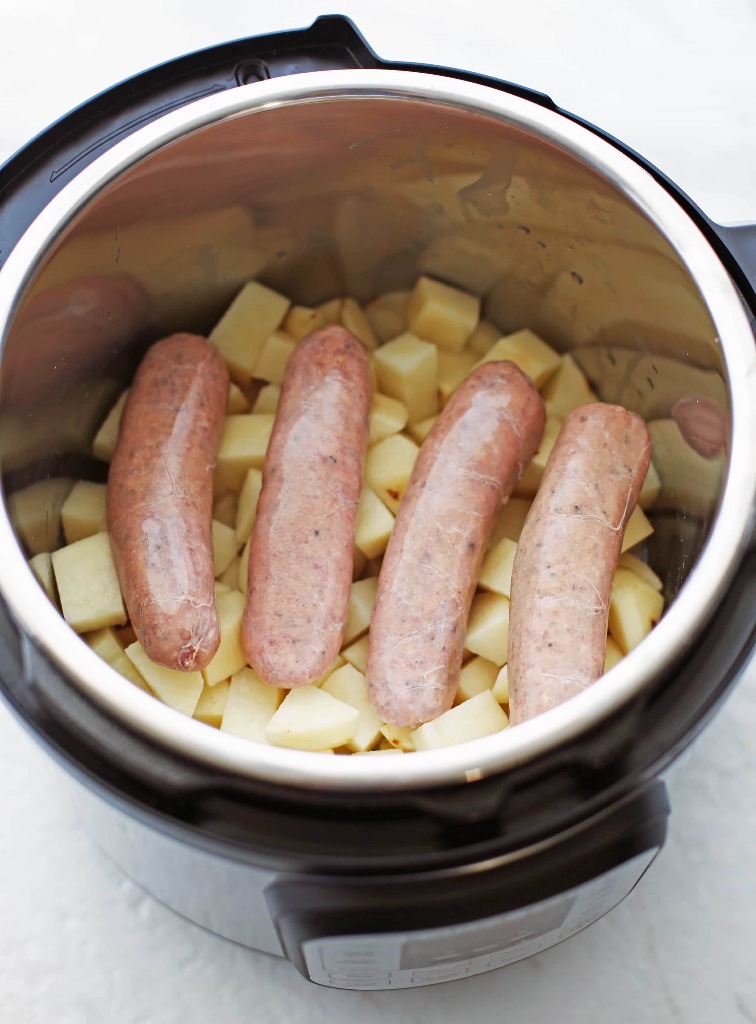 Four pork sausages on top of peeled and chopped potatoes in the Instant Pot.