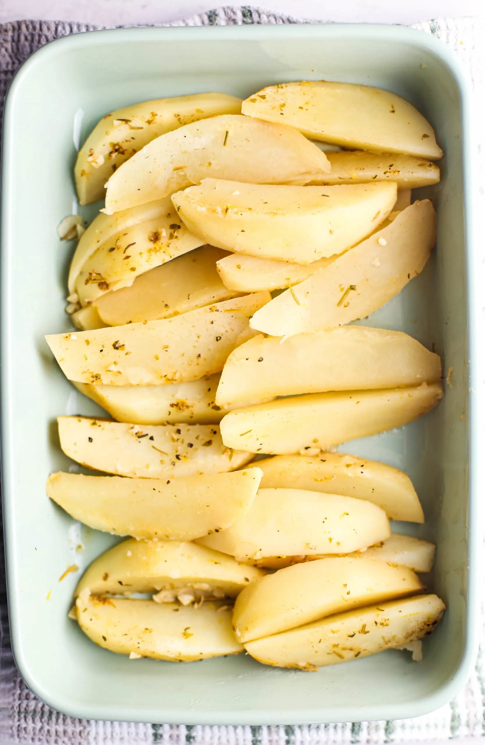 Overhead view of wedged lemon potatoes in a green casserole dish.