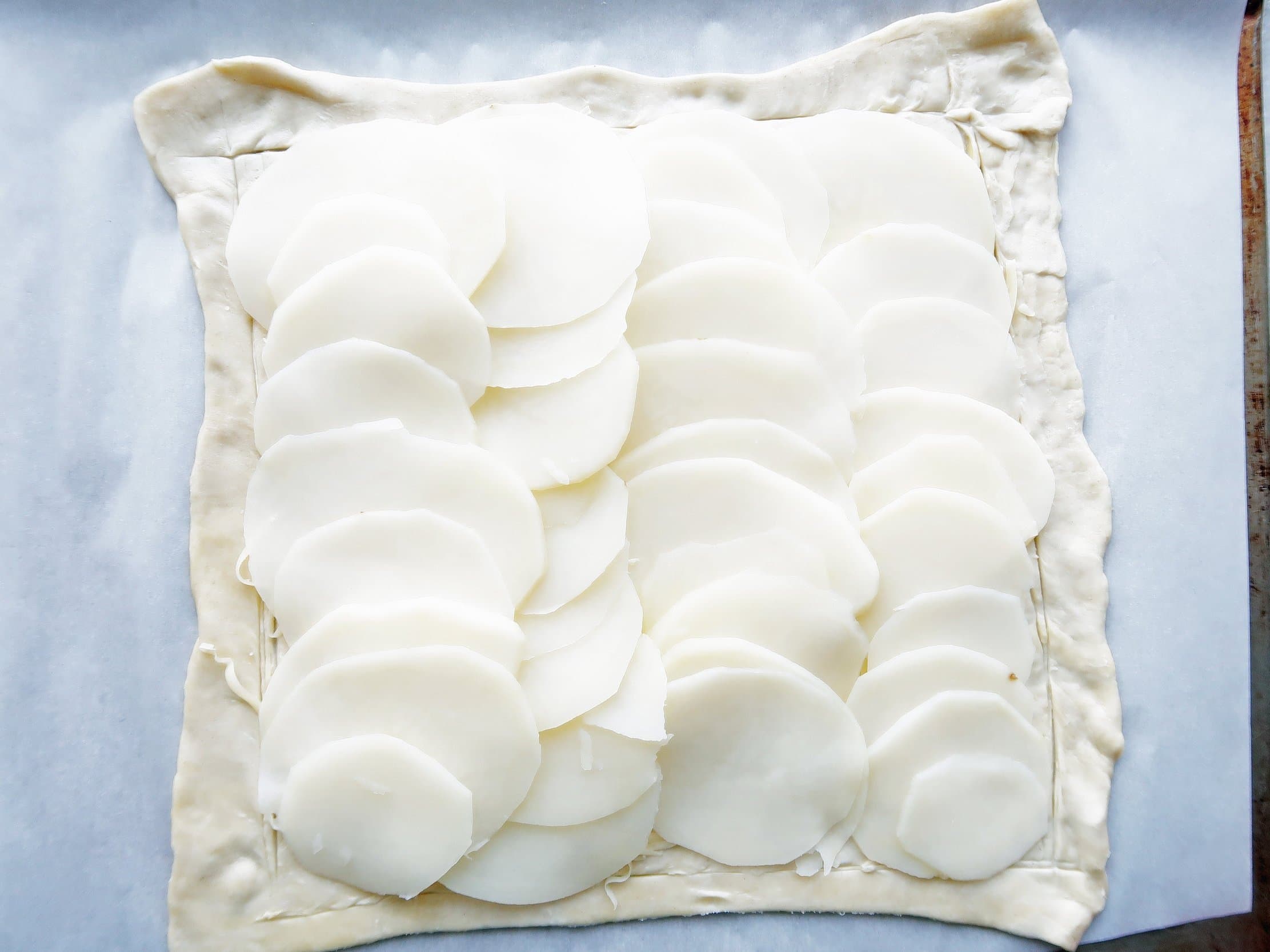 Cheese and sliced potatoes on top of a sheet of unbaked puff pastry.