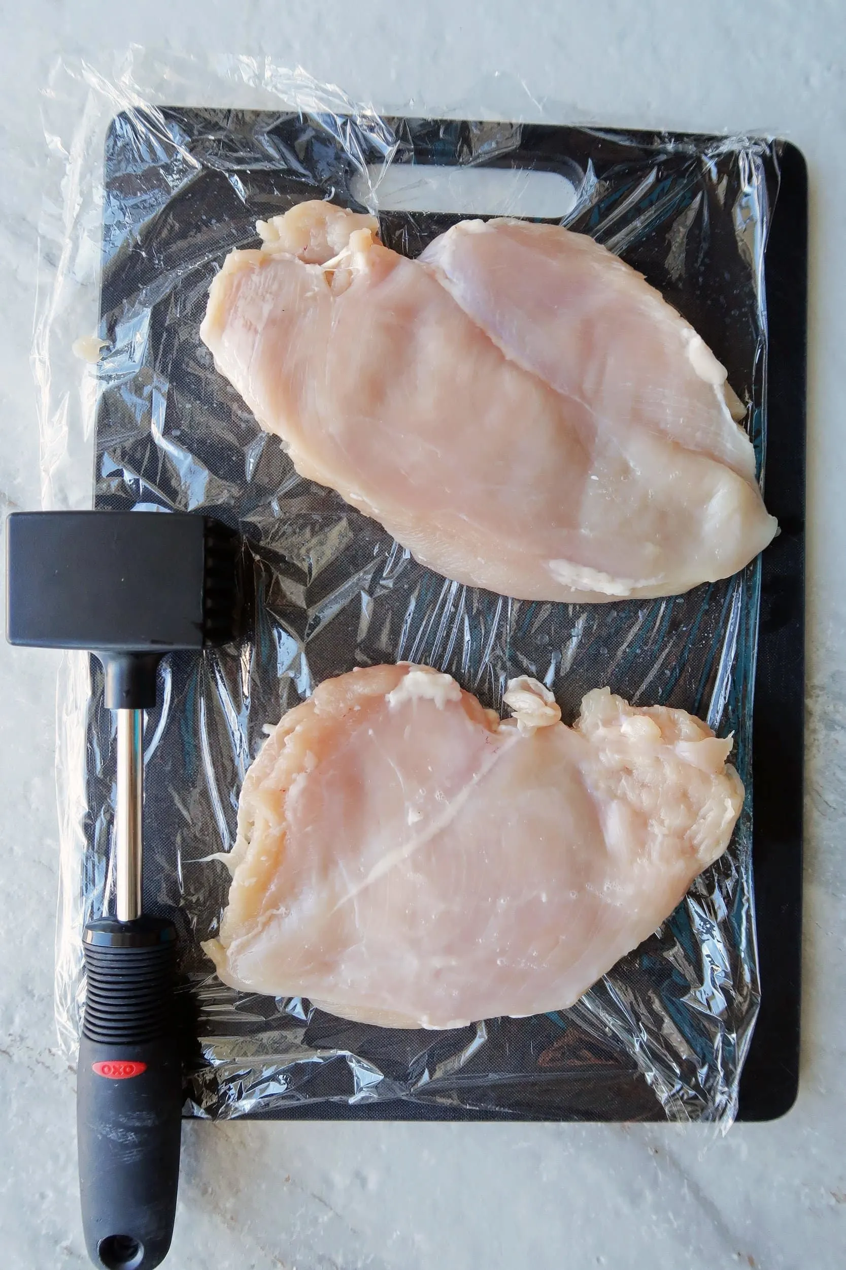Two large chicken breasts pounded to half-inch thickness on a black cutting board.