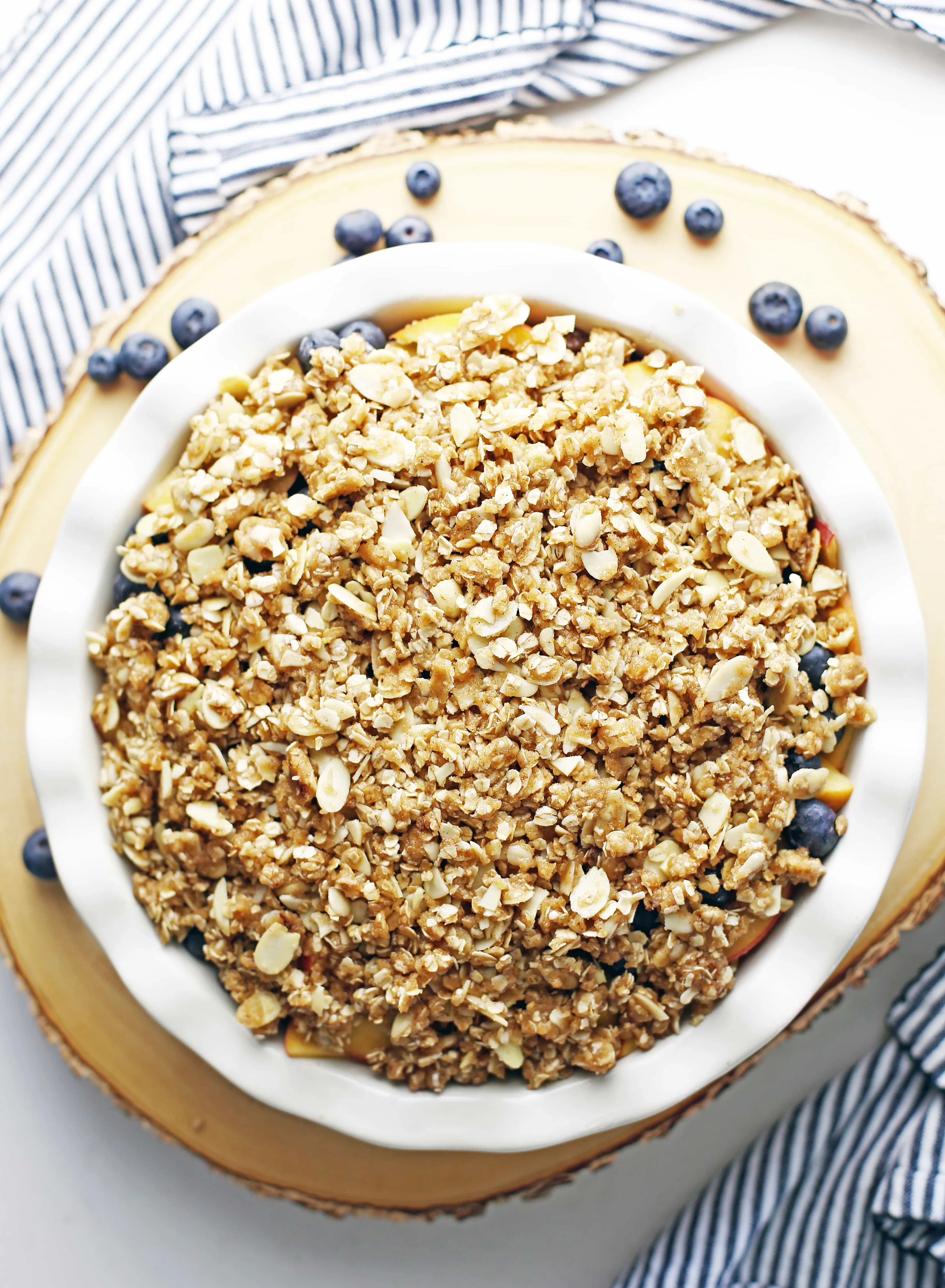 Unbaked peach blueberry crisp with almond oat topping in a round ceramic pie dish.