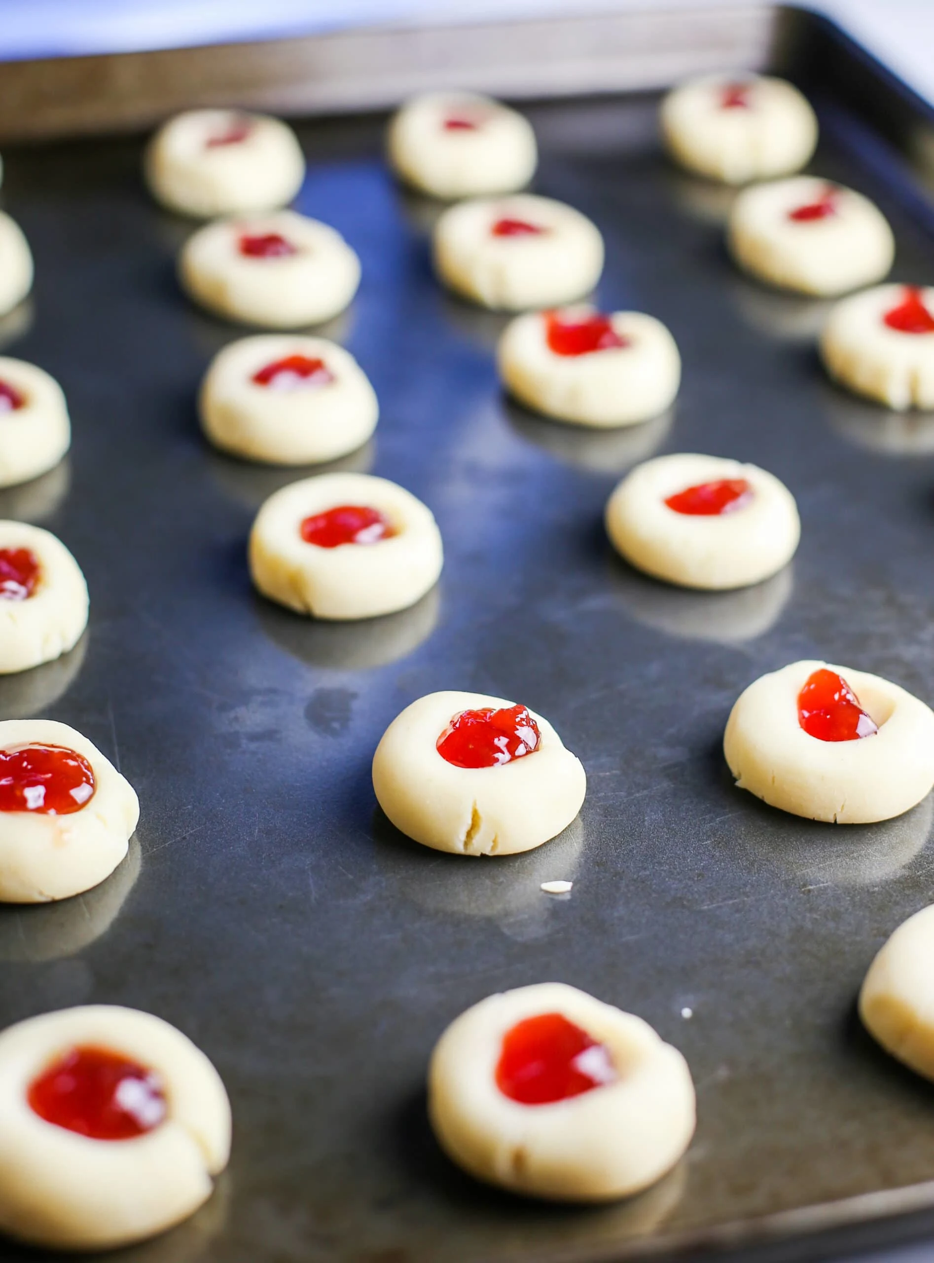 Unbaked condensed milk thumbprint cookies filled with strawberry jam on a baking sheet.