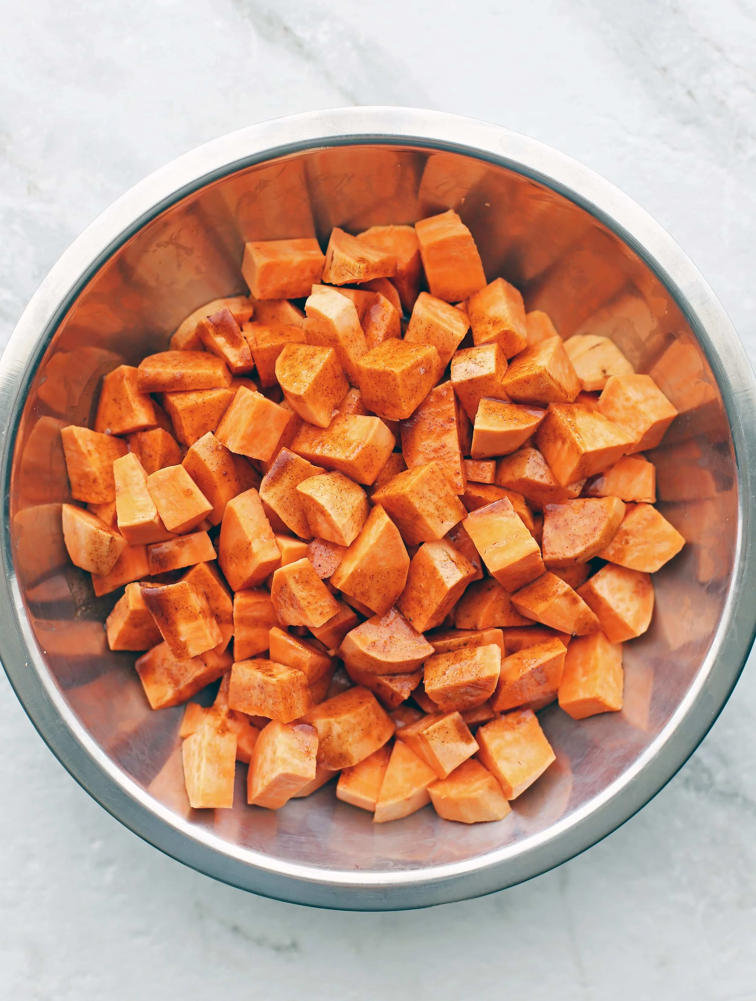 A bowl containing chunks of sweet potatoes, coconut oil, spices, and vanilla extract.