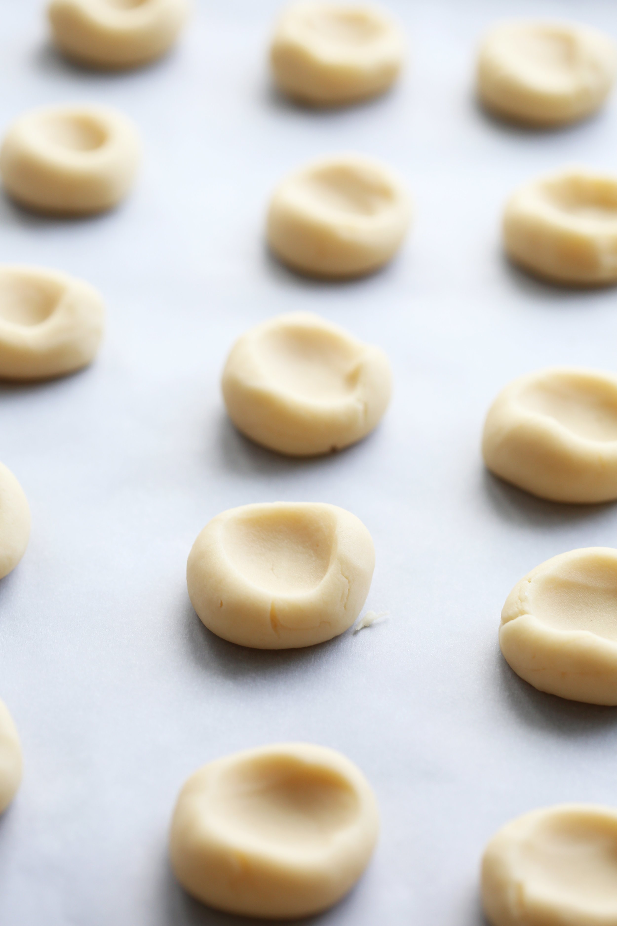 Raw shortbread cookies with a thumbprint indentation in each on a baking sheet.
