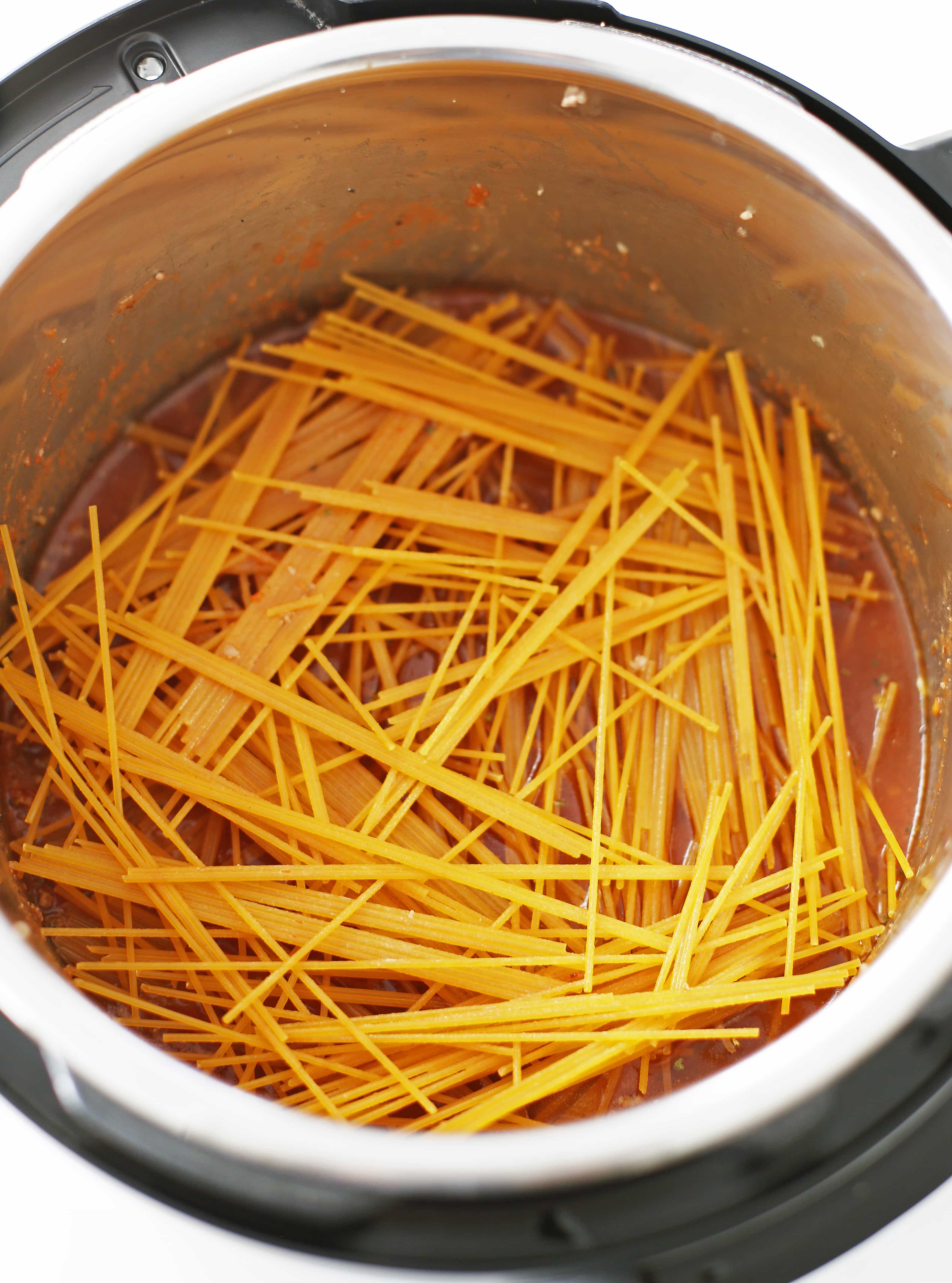 Randomly scattered dry spaghetti on top of meat sauce in the Instant Pot.