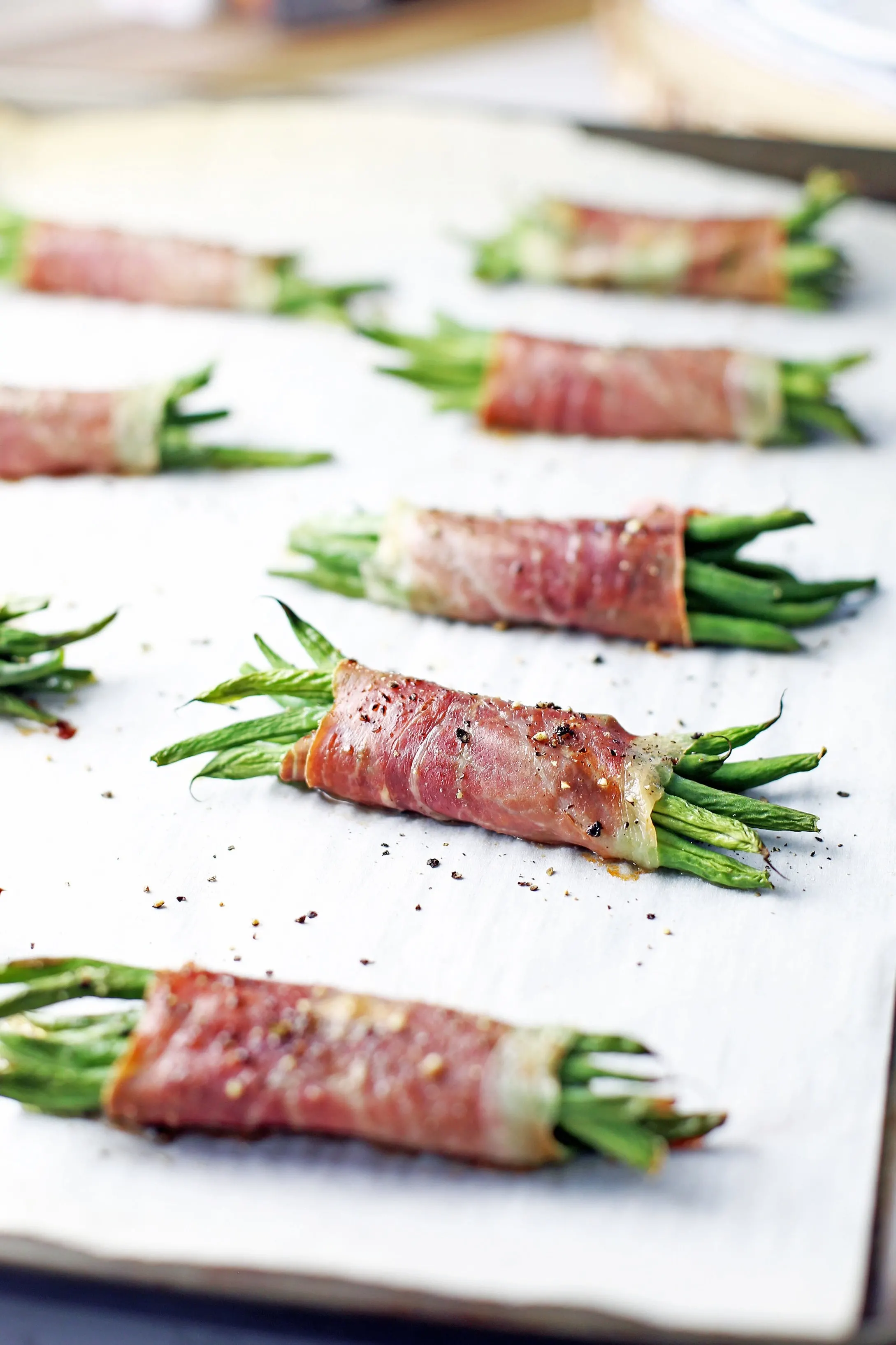 Baked crispy prosciutto wrapped green bean bundles on a large parchment paper-lined baking sheet.