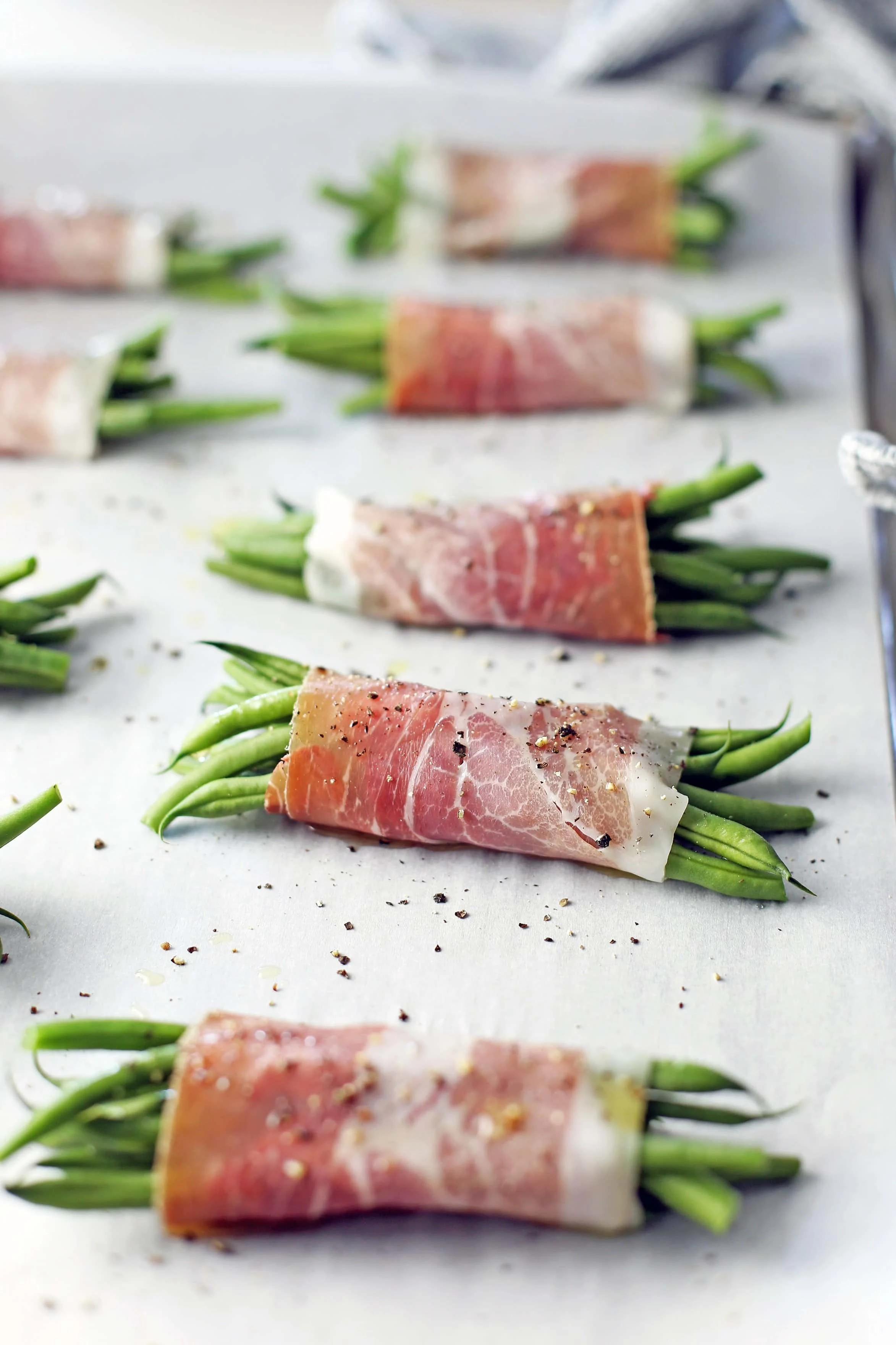 Prosciutto wrapped green beans on a large parchment paper-lined baking sheet in a single layer.