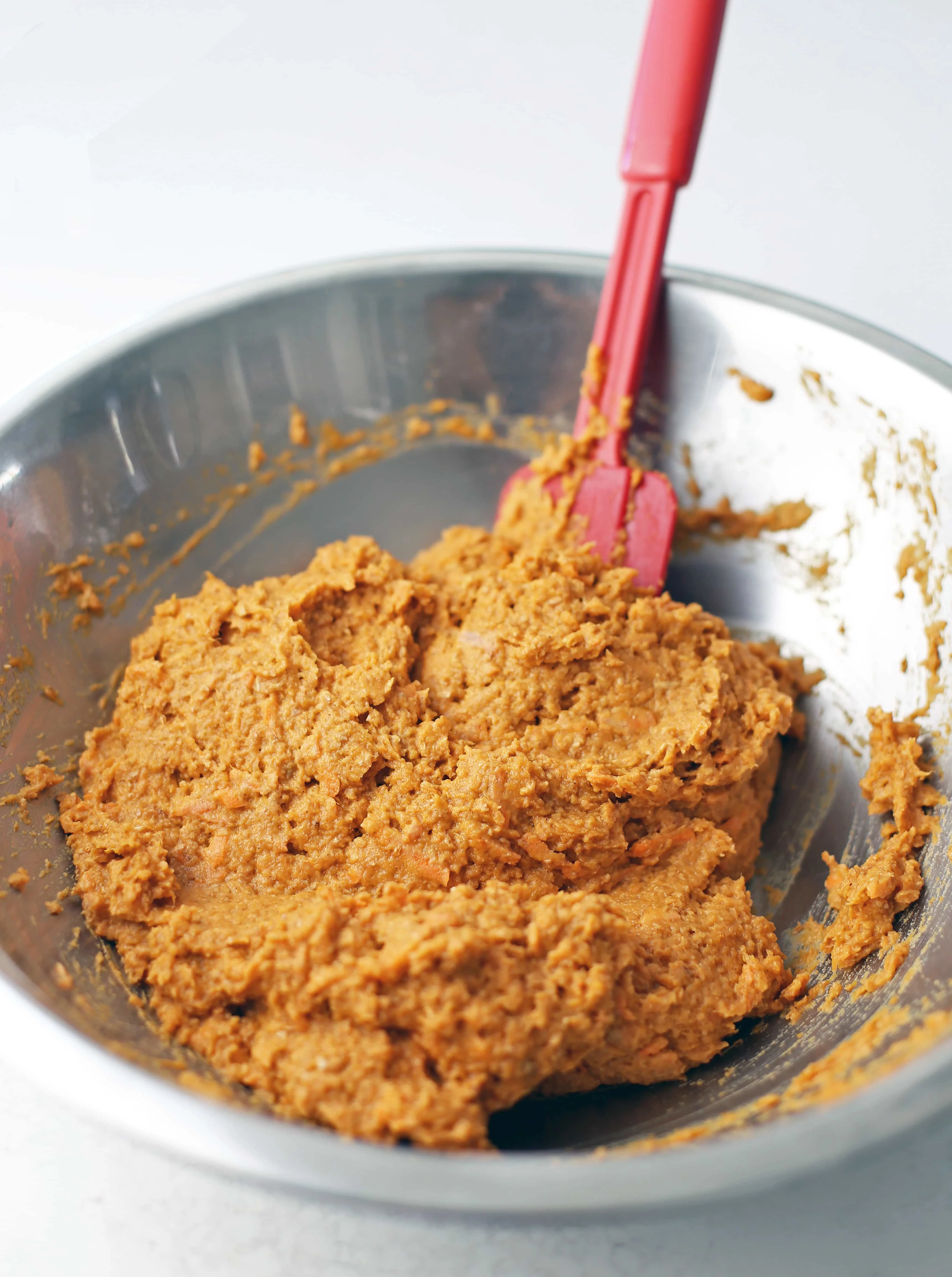 Carrot pumpkin muffin batter mixed together with a spatula in a stainless steel bowl.