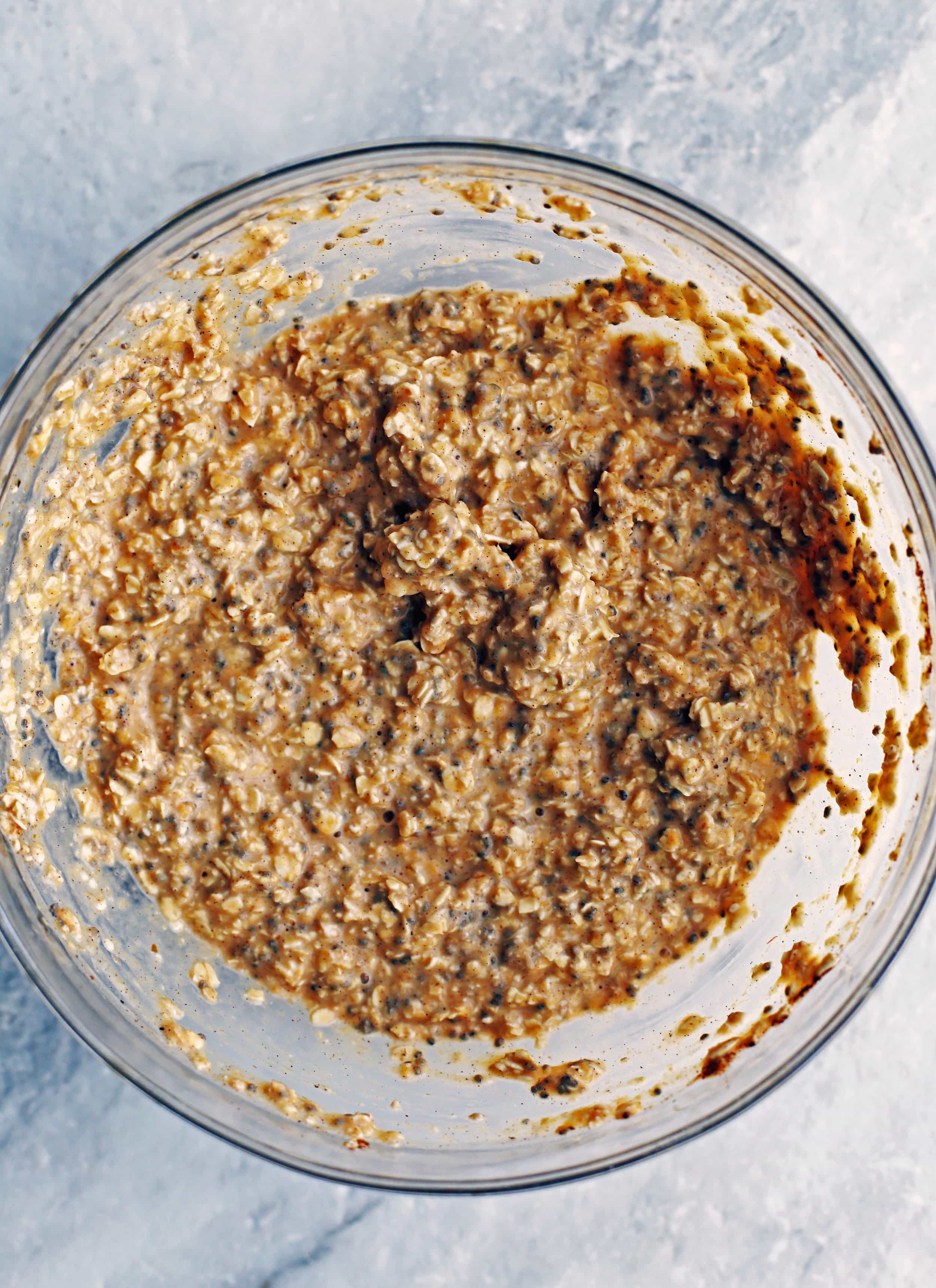 A large glass bowl containing rolled oats, pumpkin puree, chia seeds, spices, almond milk, and maple syrup all mixed together.