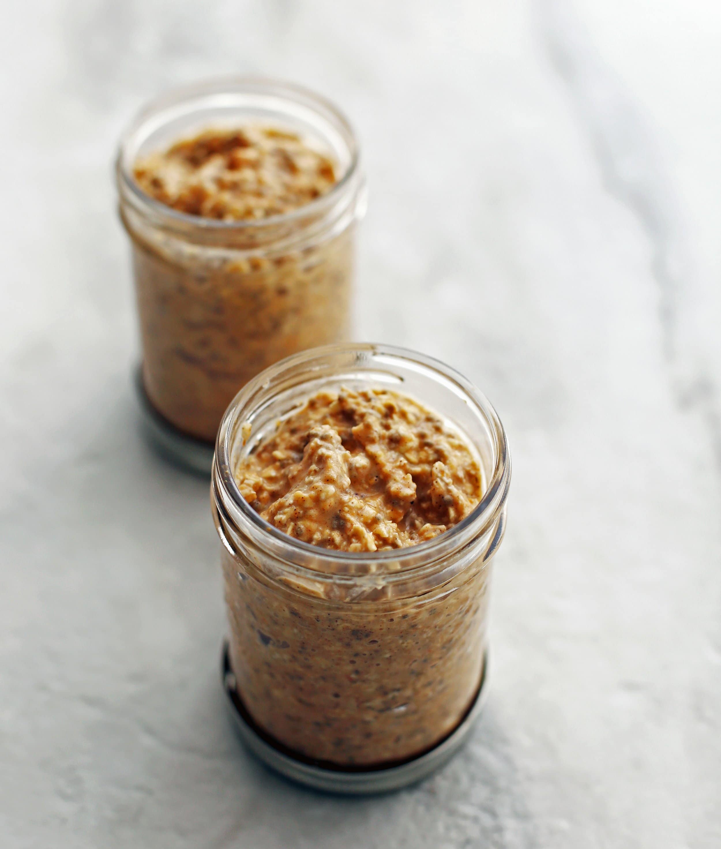 Two mason jars full of chai spiced pumpkin overnight oats on a white surface.