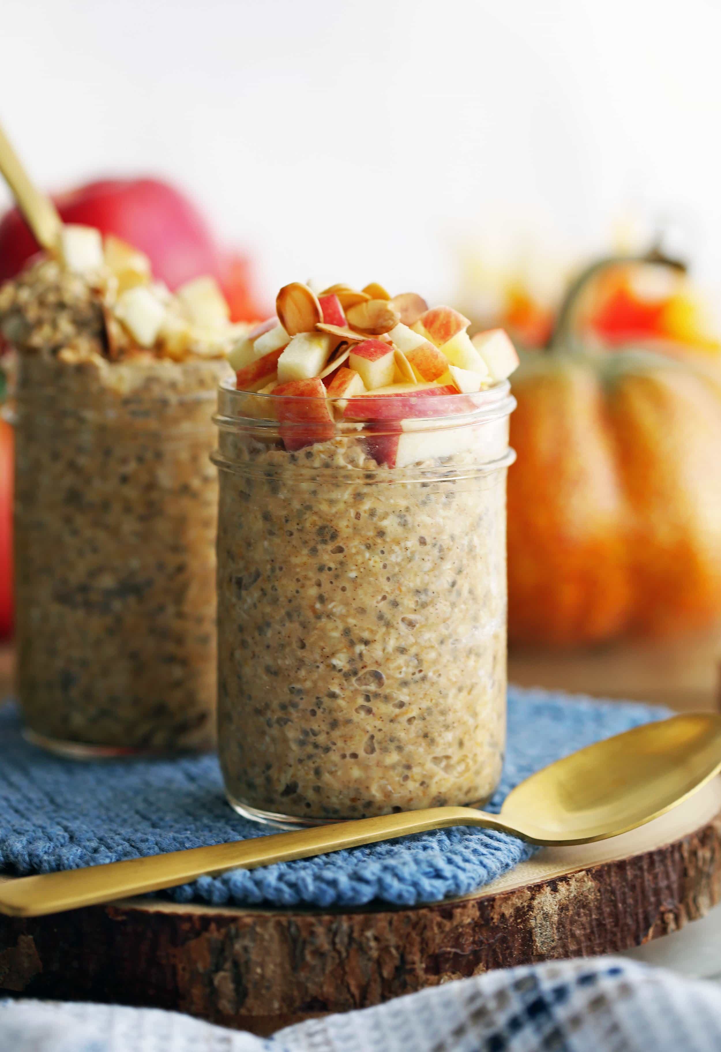 Chai spiced pumpkin overnight oats with apples and slivered almonds in two mason jars with a spoon on the side.