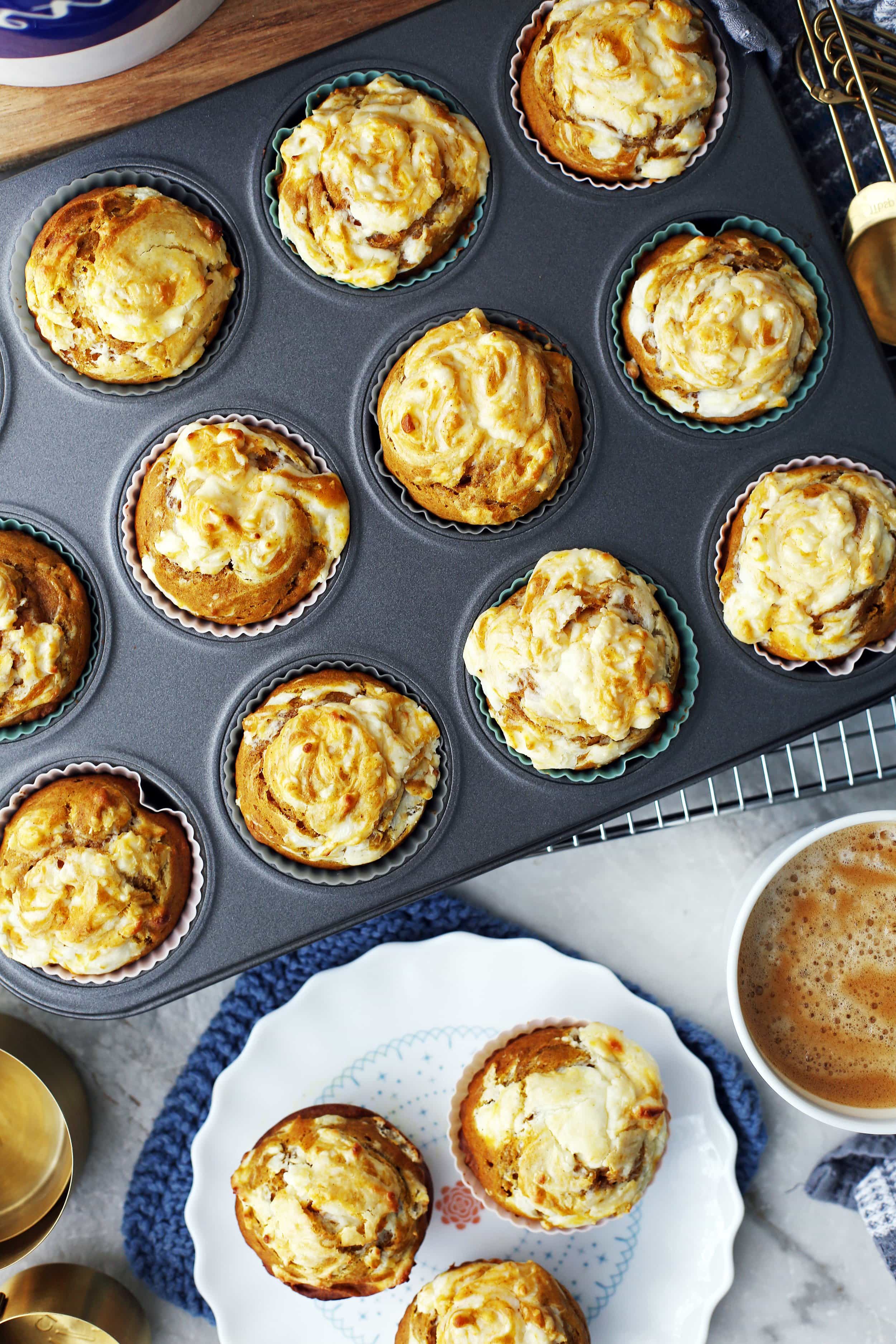 Overhead view of pumpkin cream cheese muffins in a muffin pan and on a white plate.