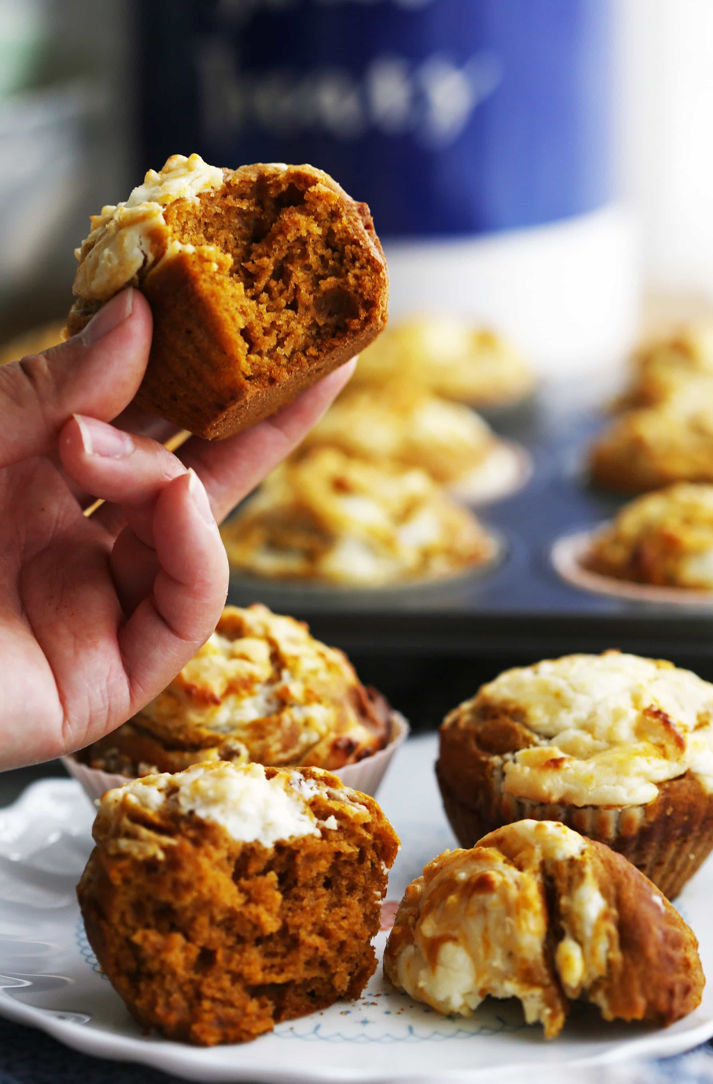 A hand holding a pumpkin cream cheese muffin with a bite taken out of it.