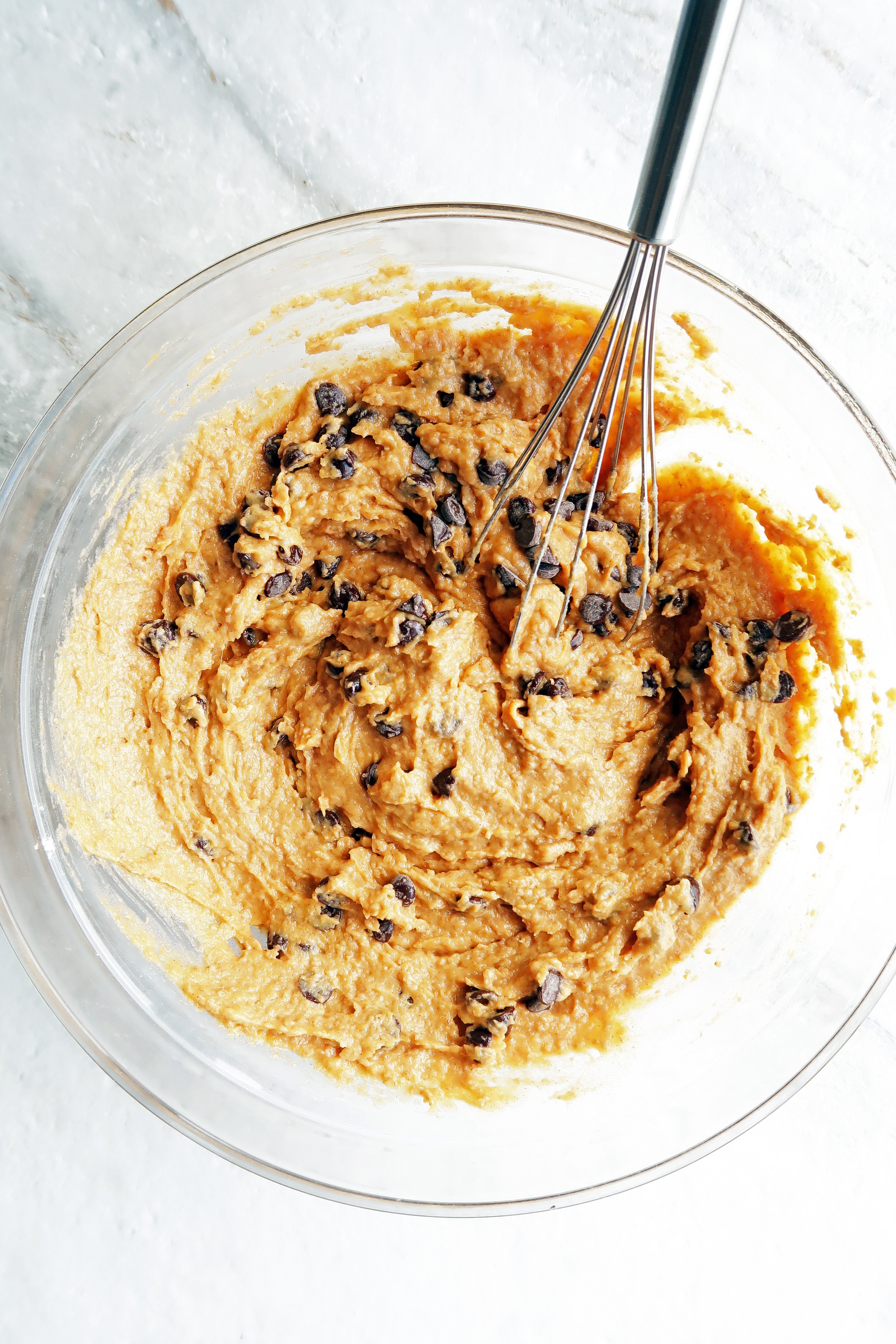 Pumpkin chocolate chip whole wheat muffin batter in a glass bowl with a metal whisk.