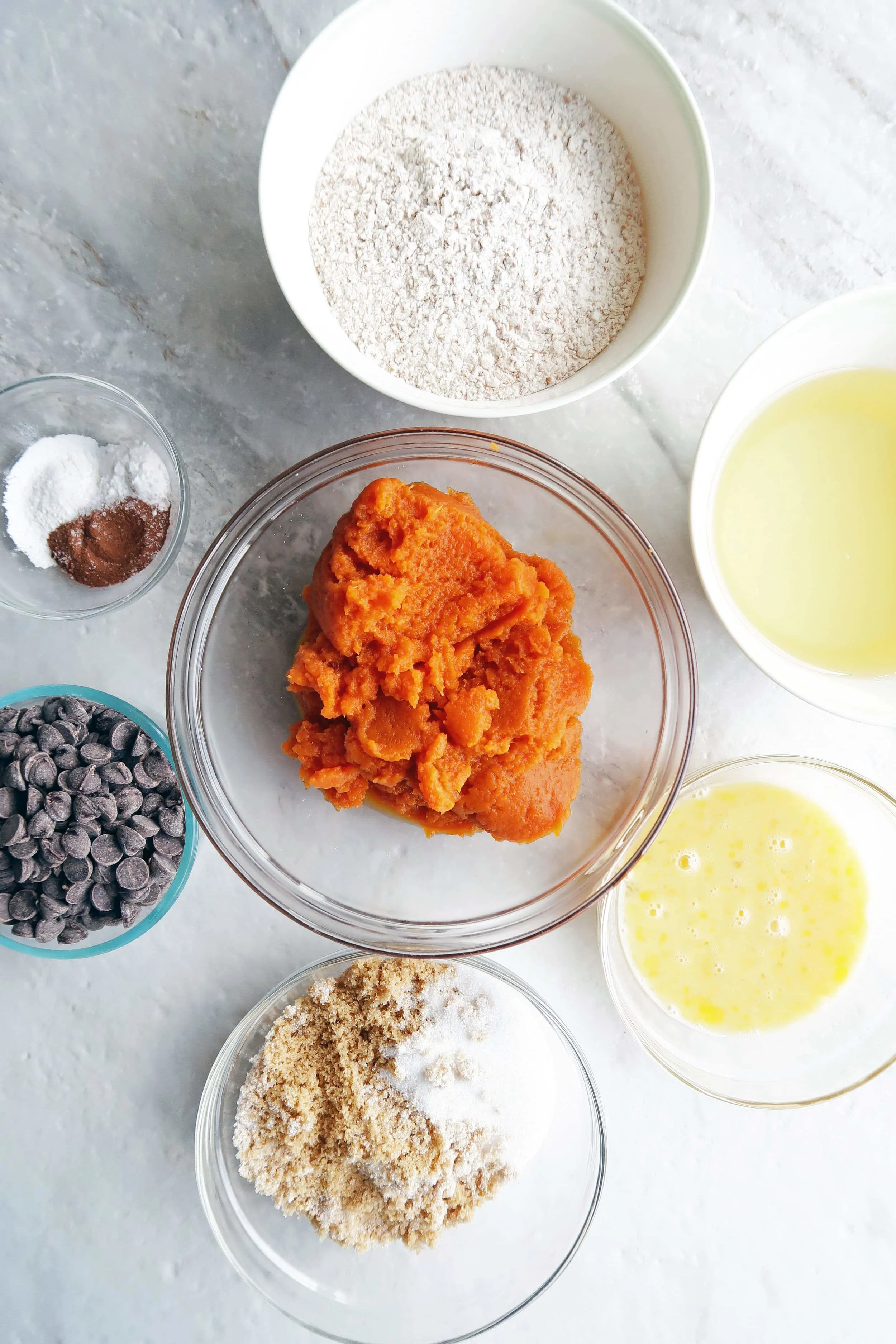 Bowls of chocolate chips, sugar, oil, pumpkin puree, baking soda, baking powder, spices,and eggs.