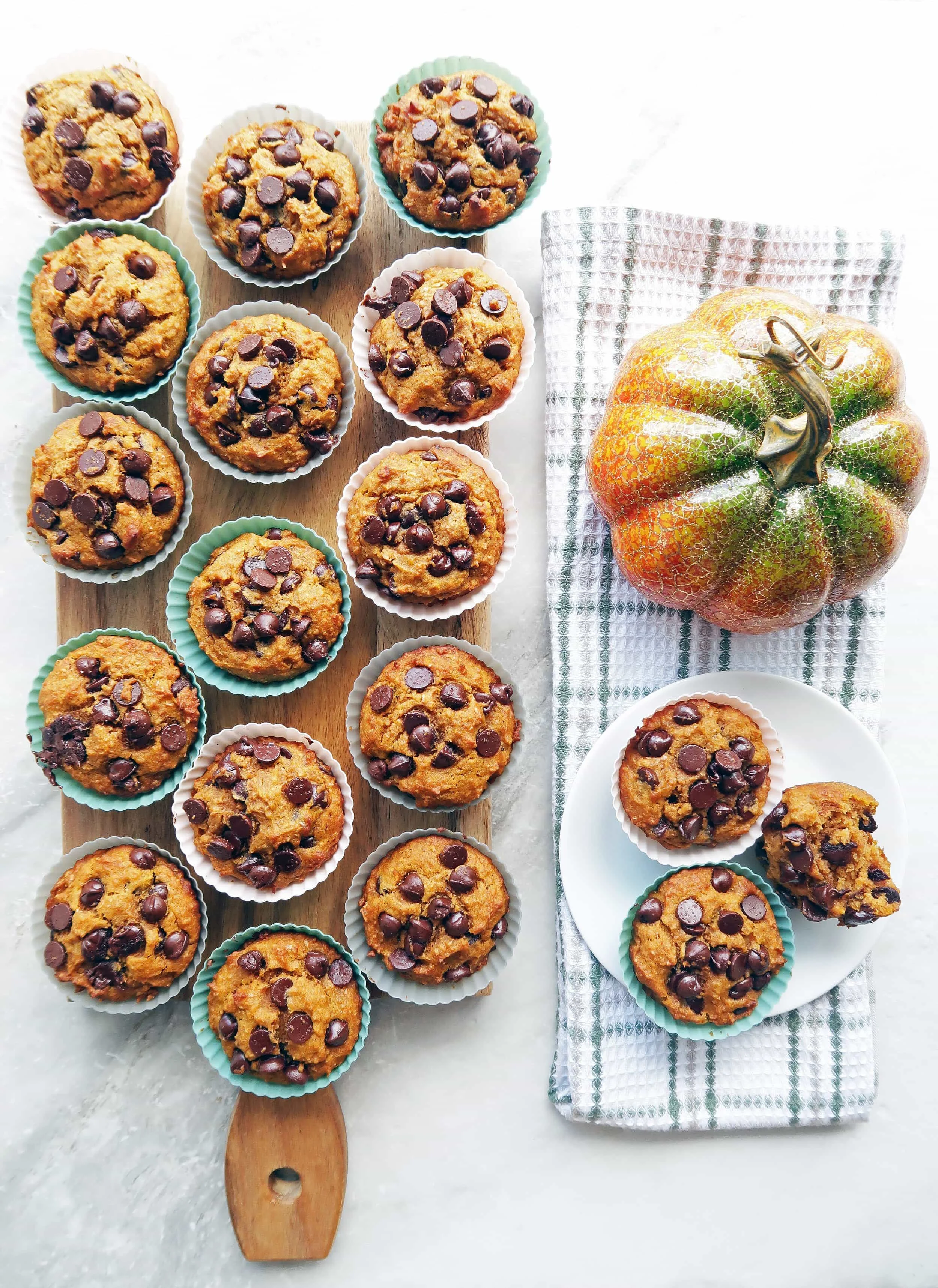 Pumpkin chocolate chip whole wheat muffins placed on a rectangular wooden board and on a white plate.