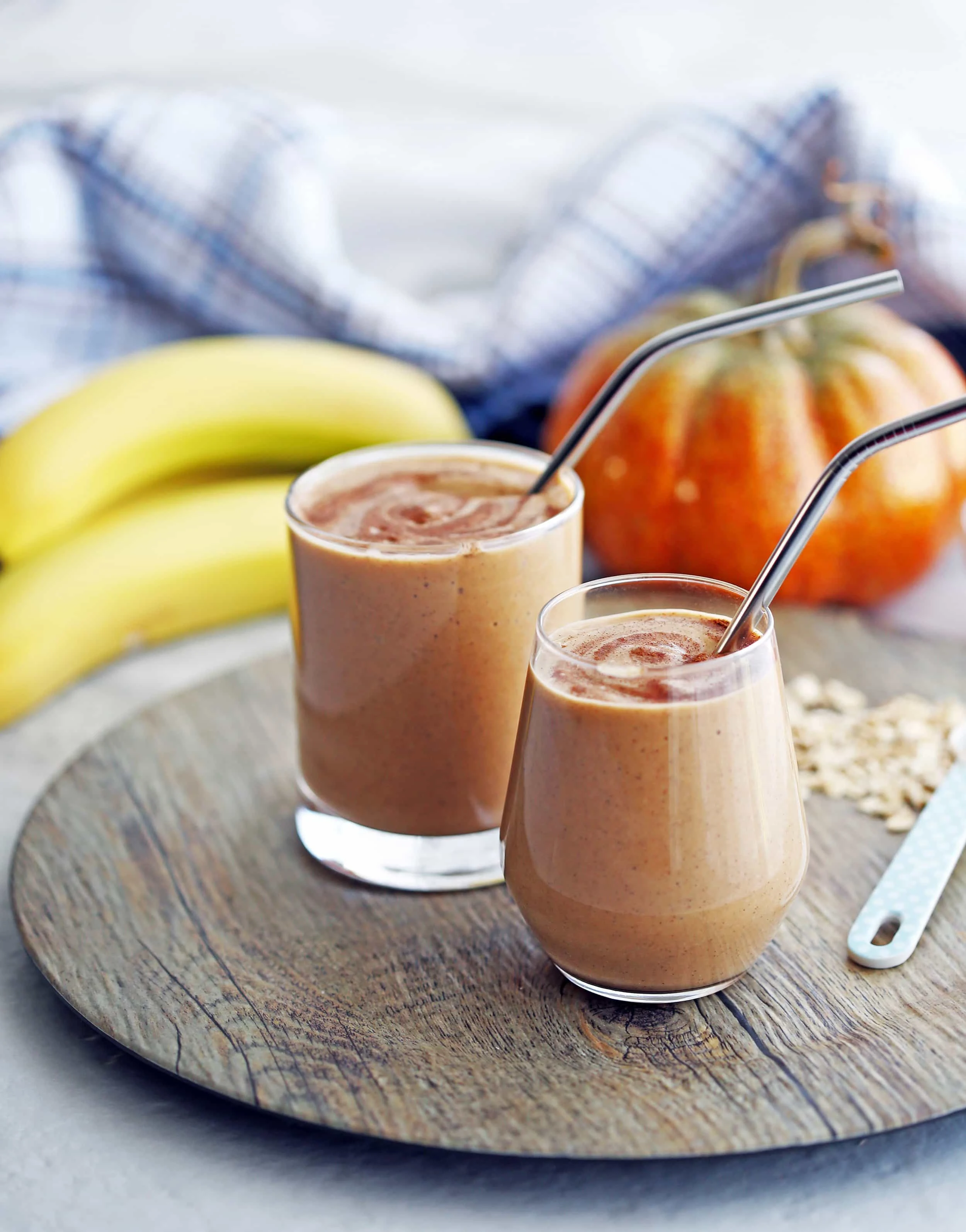 Two glasses of pumpkin pie spice protein smoothies with banana and pumpkin decor in the background.