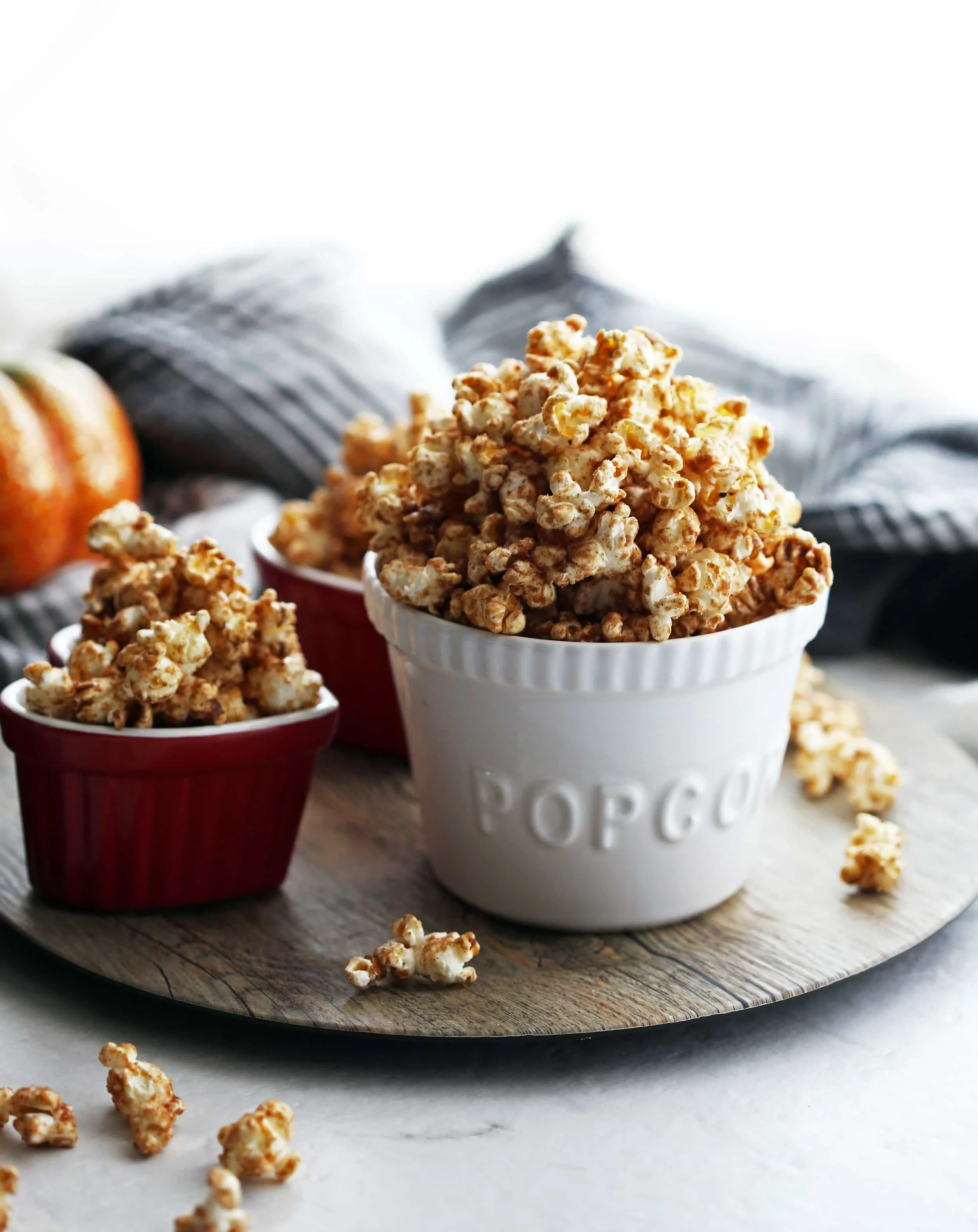 Side view of homemade pumpkin spice butterscotch popcorn in a three bowls with popcorn scattered everywhere.