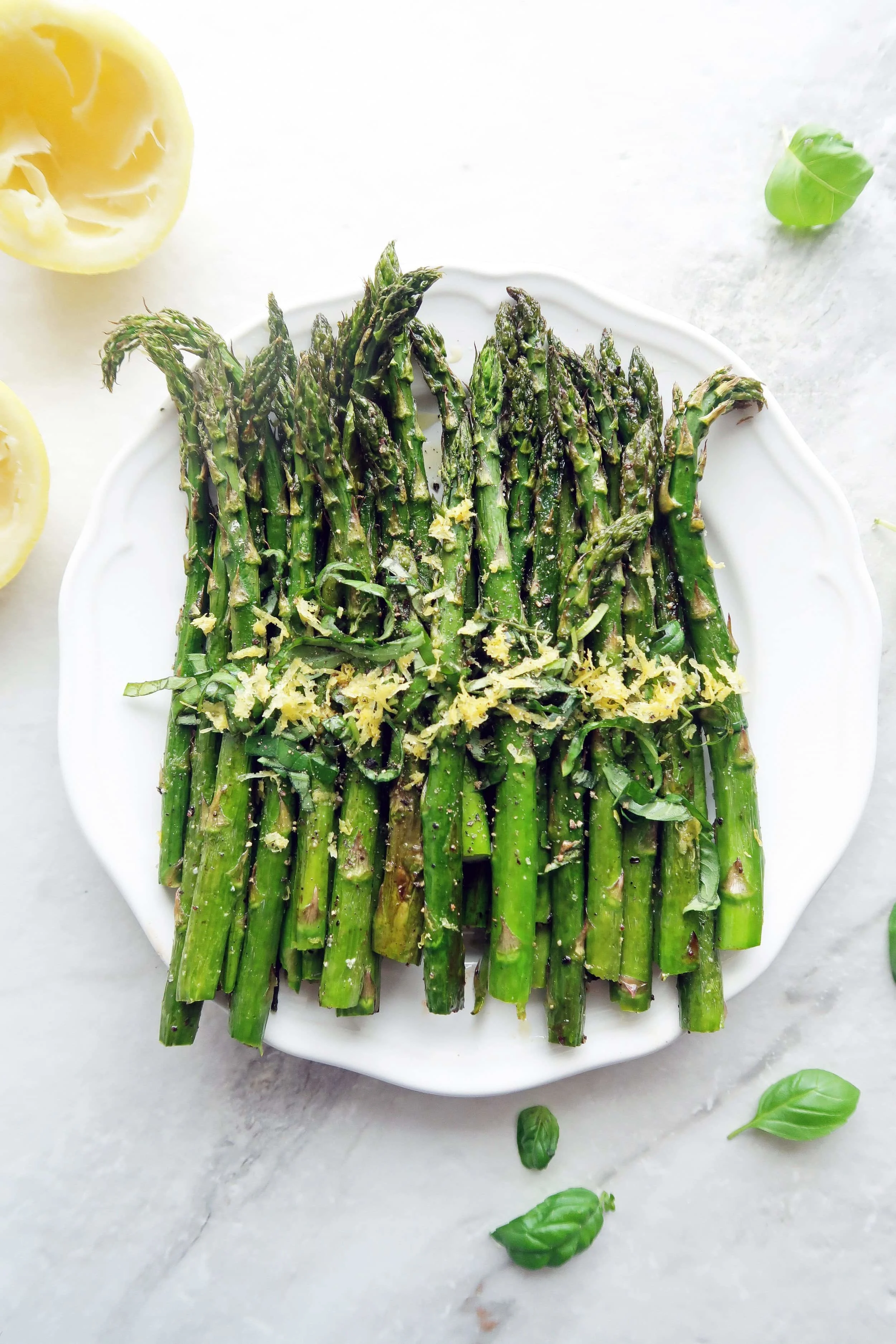 Quick Roasted Asparagus with lemon zest and sliced basil on a white plate with fresh basil leaves around it.