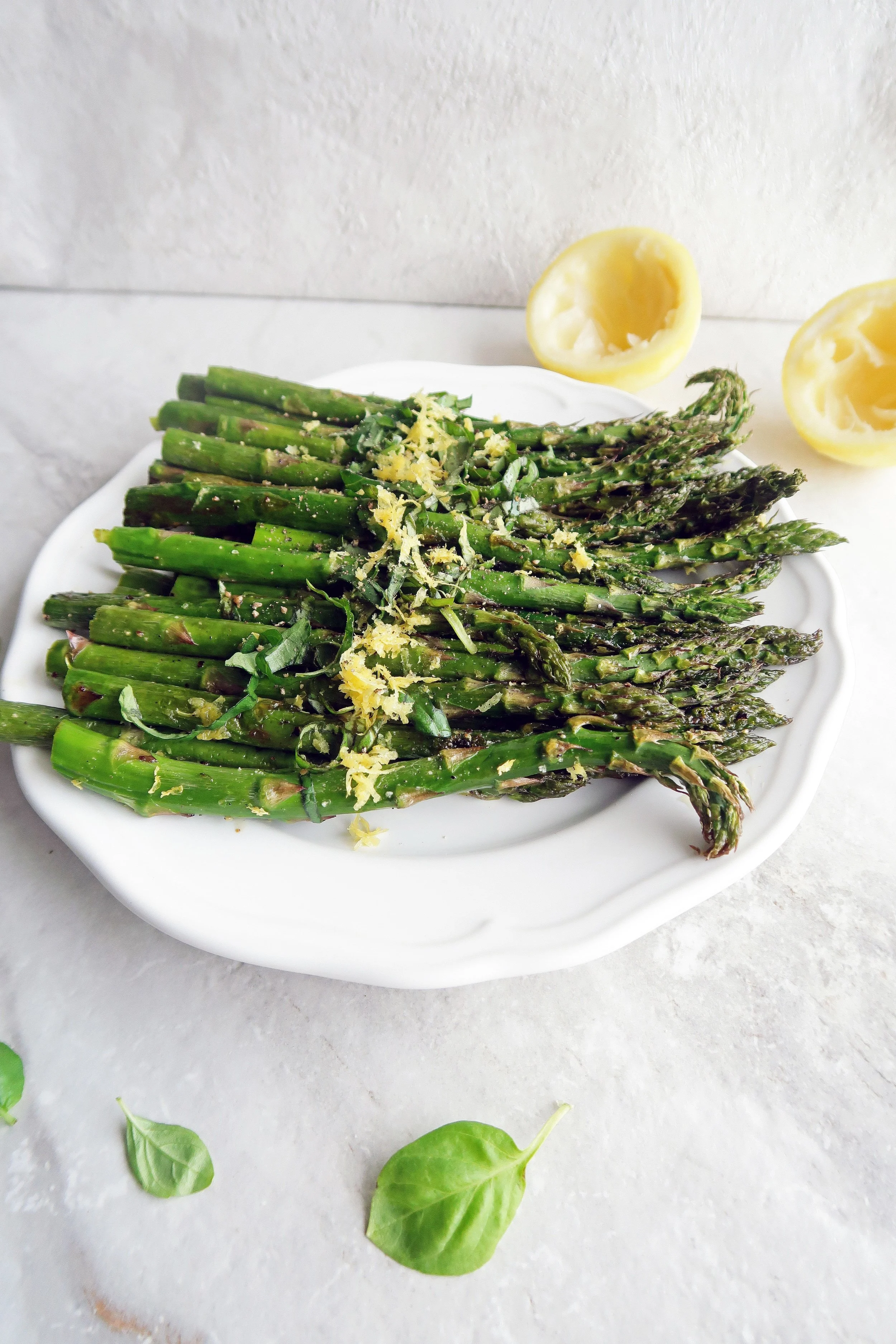 Vegan and gluten-free roasted asparagus with lemon and fresh basil on a white plate.