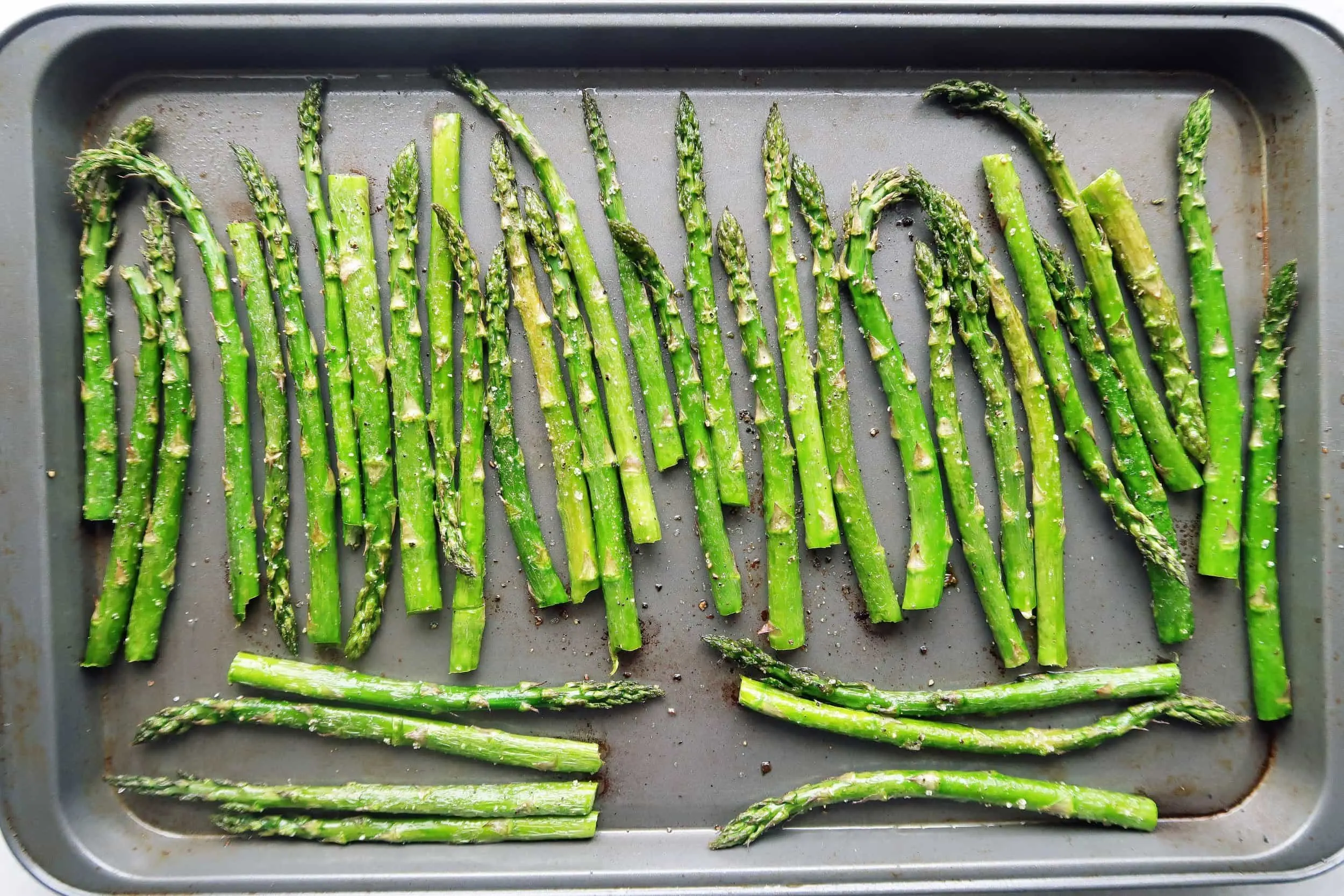 Asparagus coated with olive oil, salt, and pepper, lined up on a sheet pan, ready for roasting.