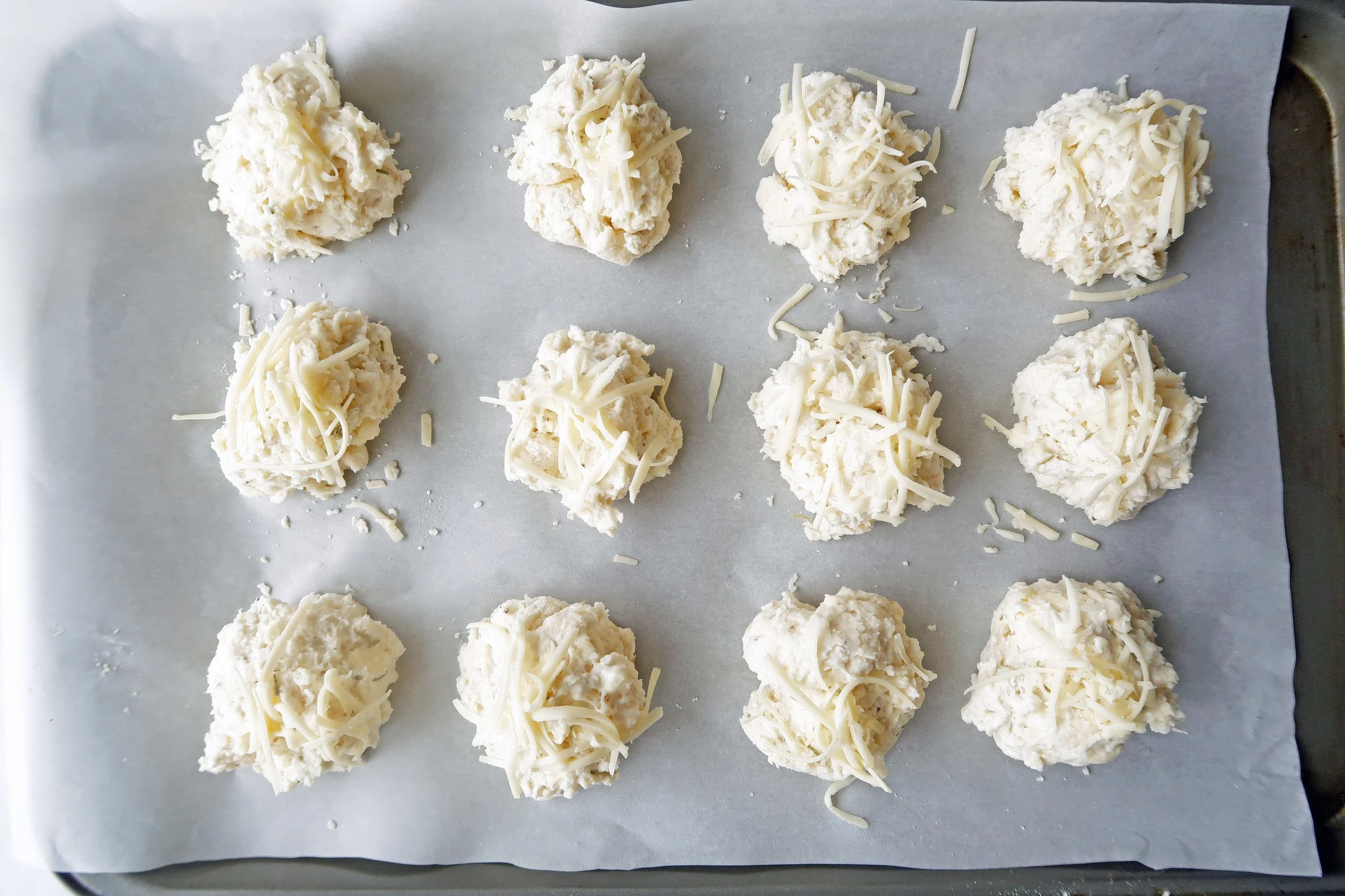 Rosemary cheddar biscuits on a baking sheet, cheese sprinkled on top, ready for the oven.