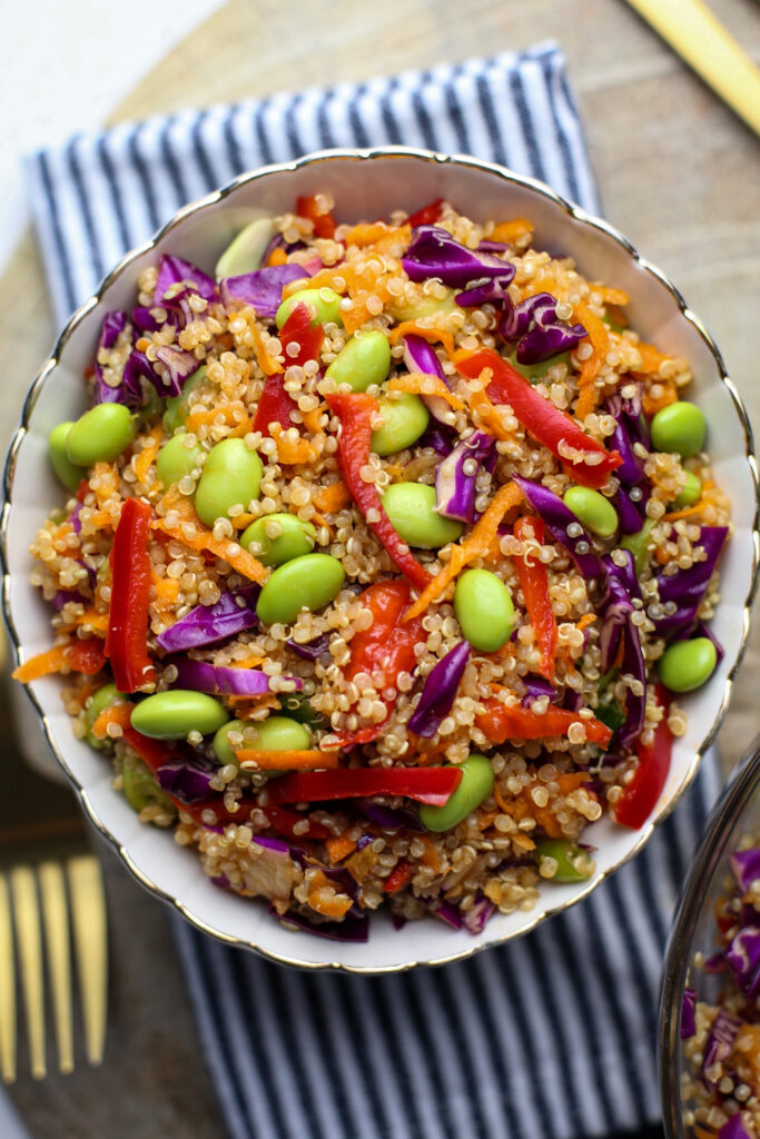 Quinoa edamame salad with peppers, cabbage, and carrots in a scalloped bowl.