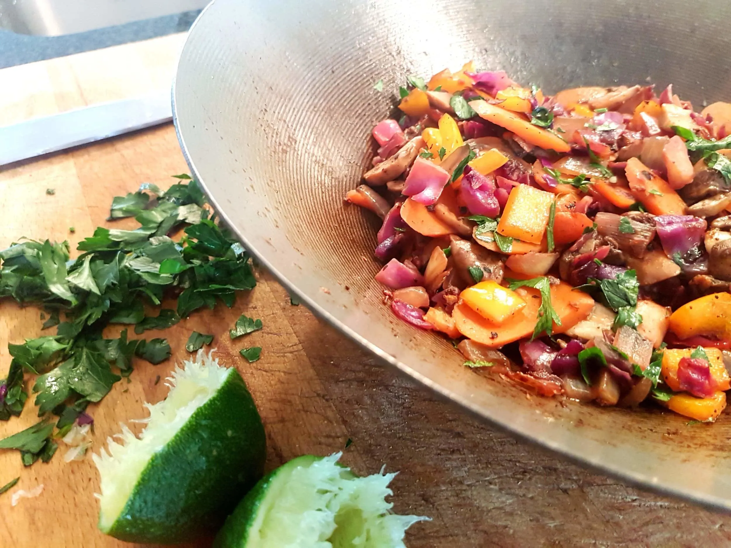 Freshly cooked vegetables in a wok with parsley and lime.