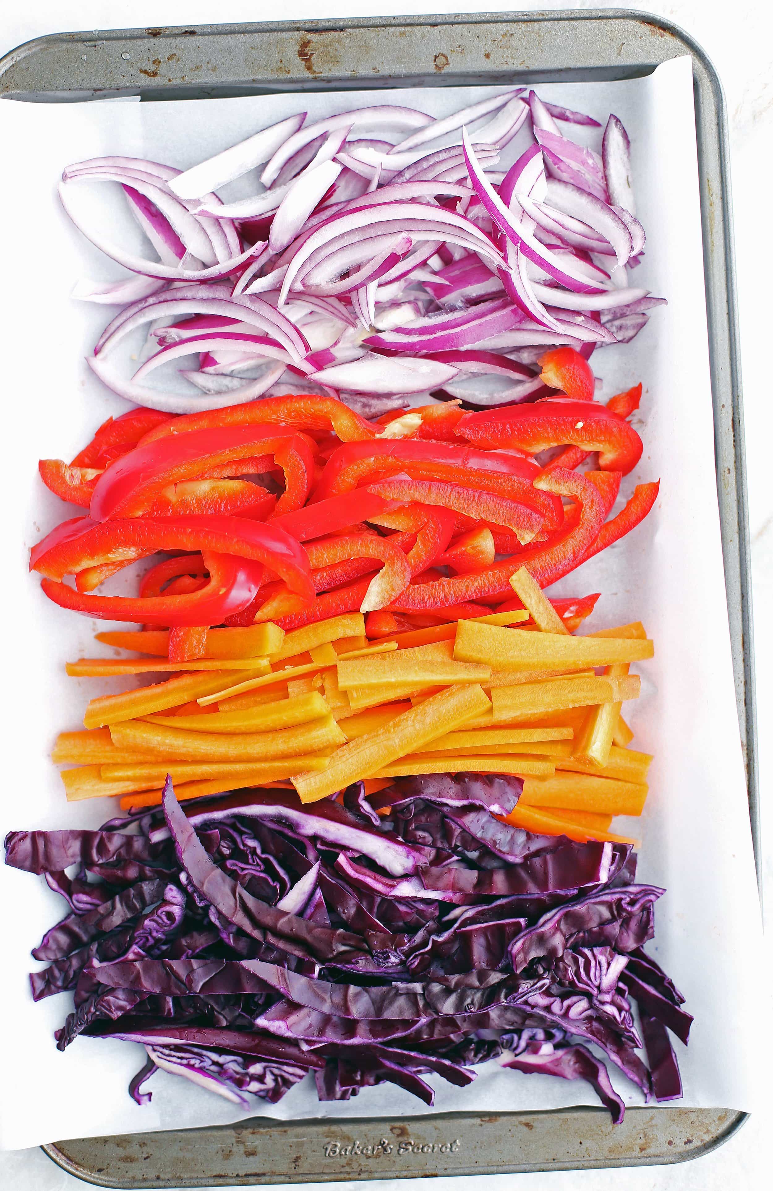 Sliced red cabbage, carrots, red bell pepper, and red onion on a baking sheet.