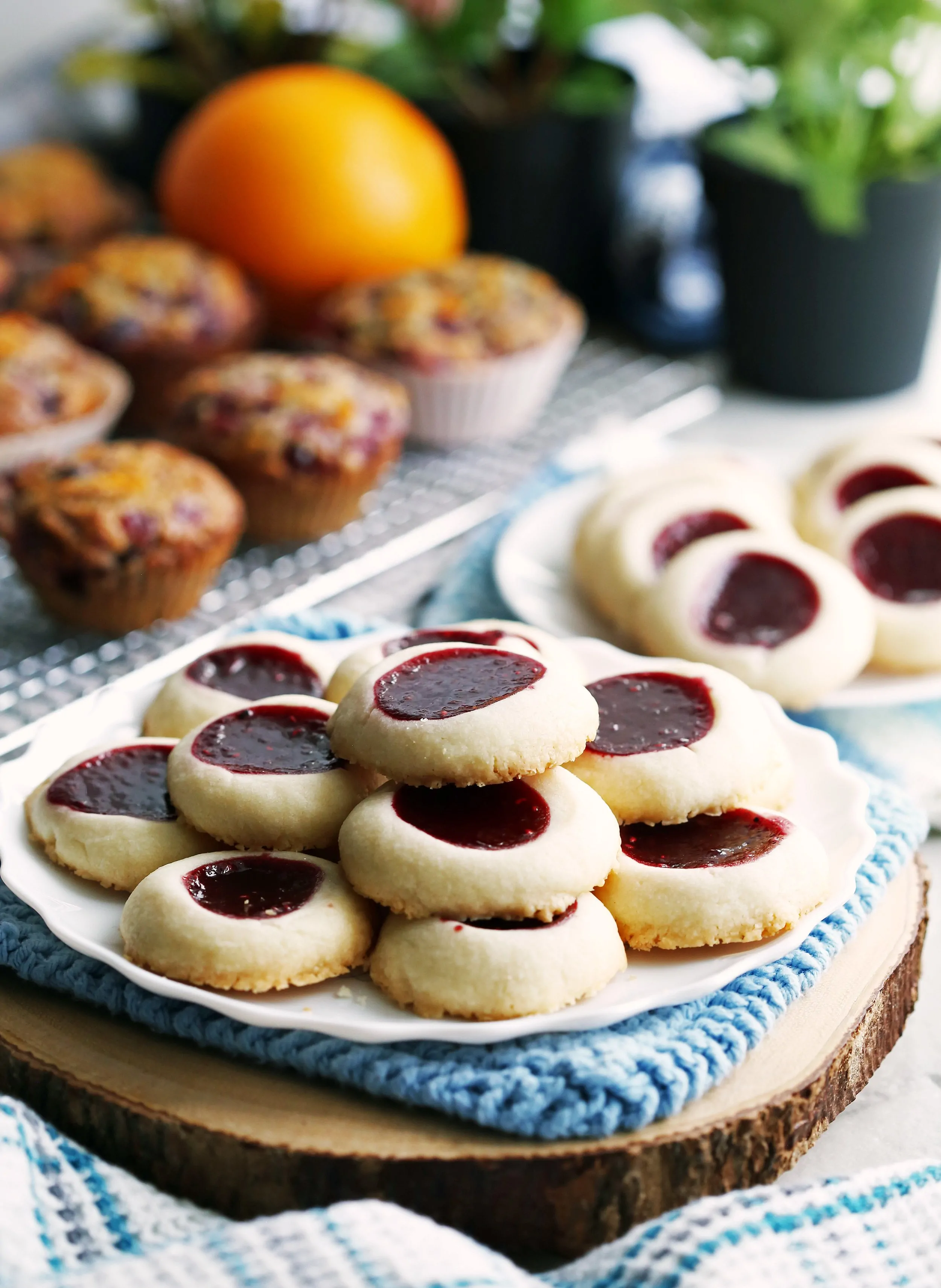 Two white plates containing raspberry shortbread thumbprint cookies that are stacked on top of one another.