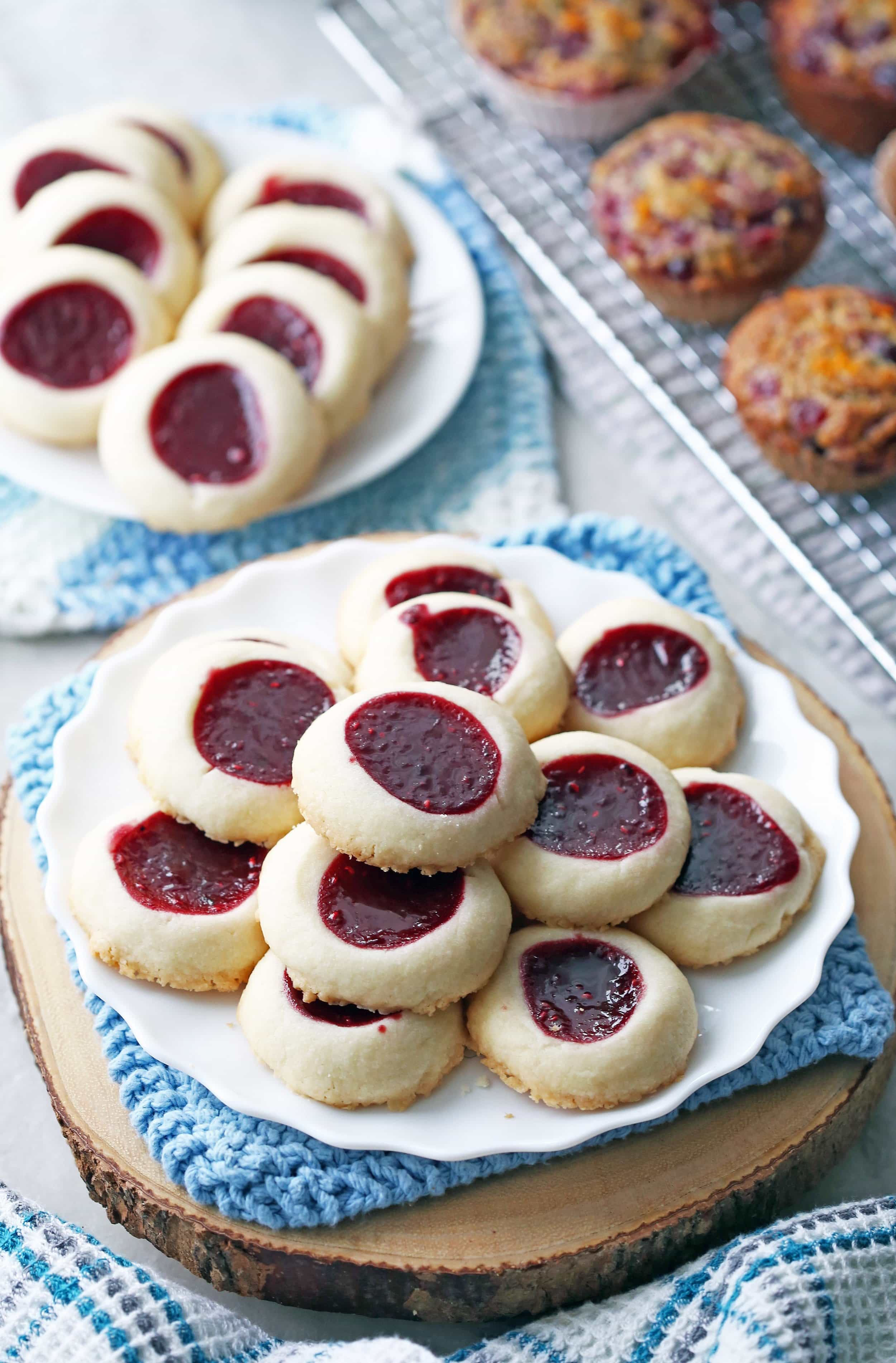 Raspberry shortbread thumbprint cookies stacked on two white plates.