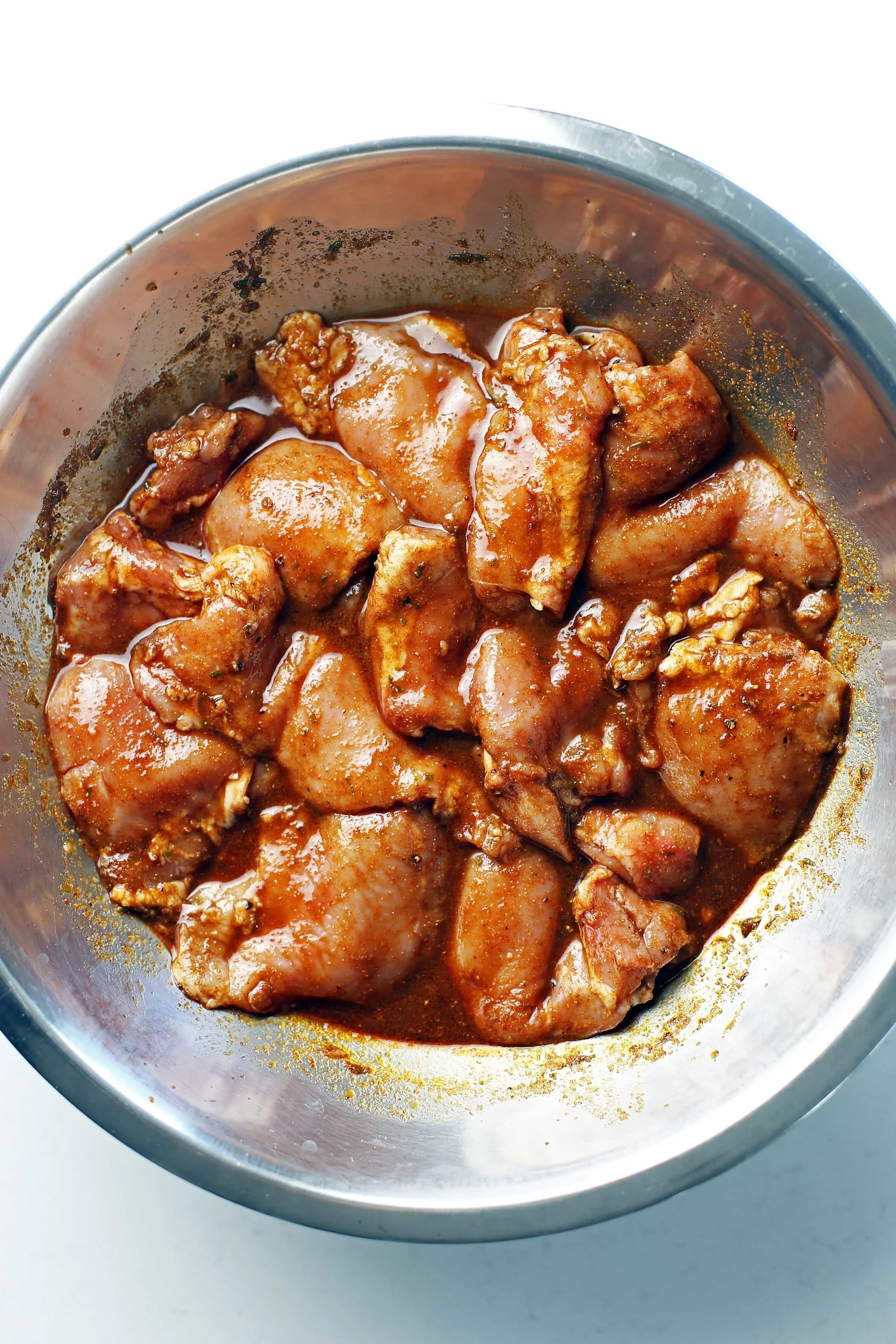 Raw boneless skinless chicken thighs in a balsamic chili lime sauce in a large stainless steel bowl.