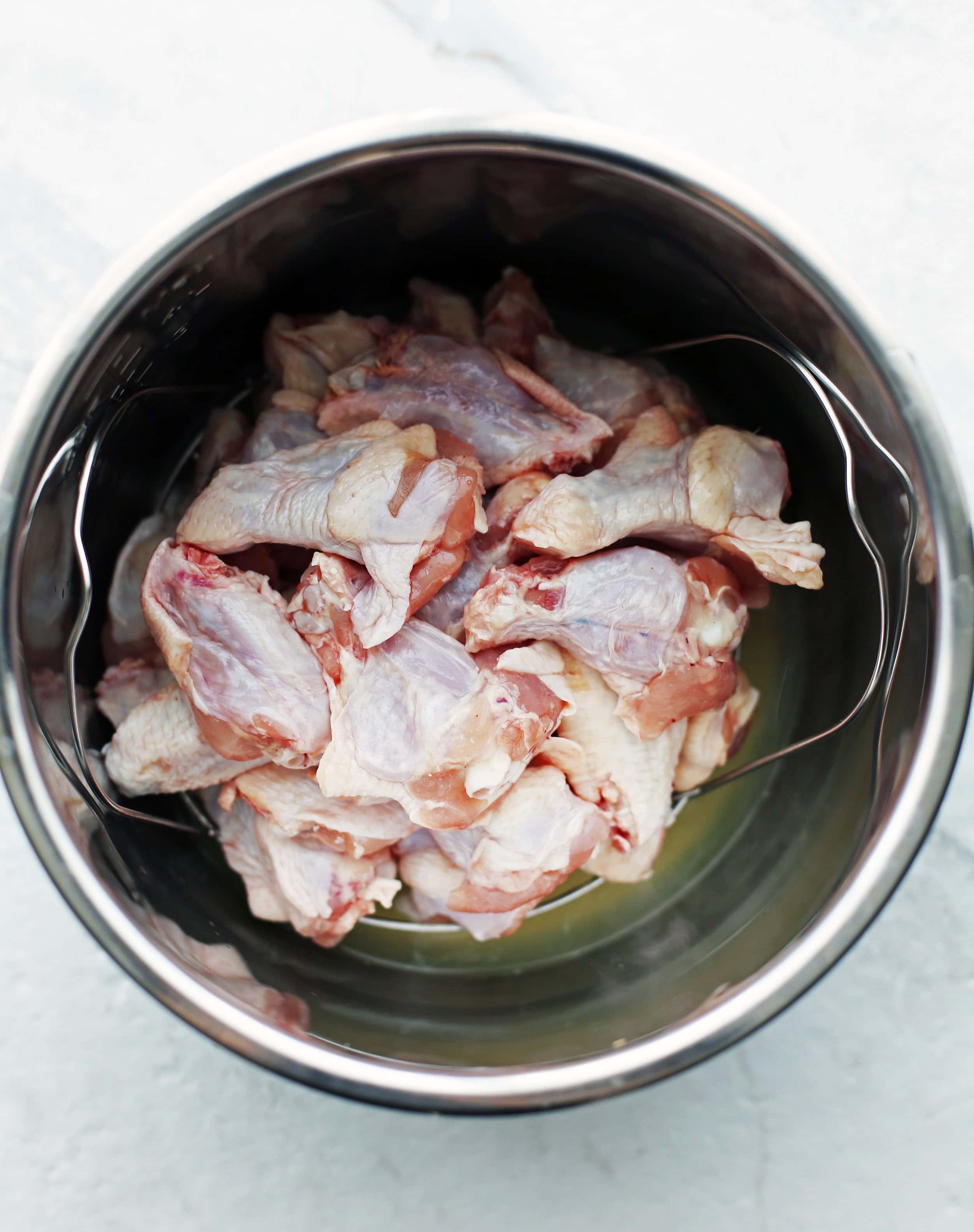 In the Instant Pot, a shallow layer of water and orange juice mixture in the pot with raw chicken wings piled onto top of a metal trivet.