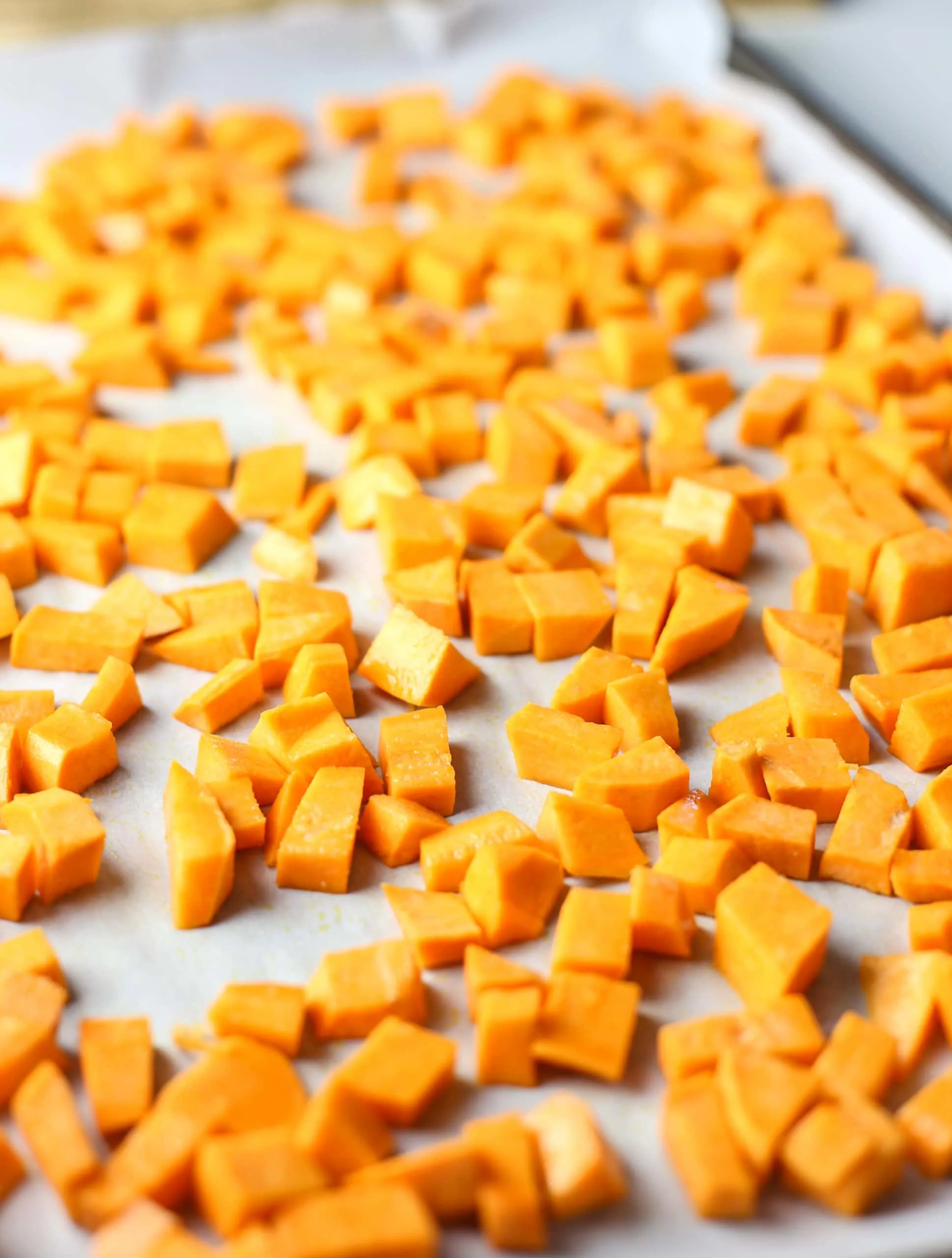 Chopped raw butternut squash on a parchment paper lined baking sheet.