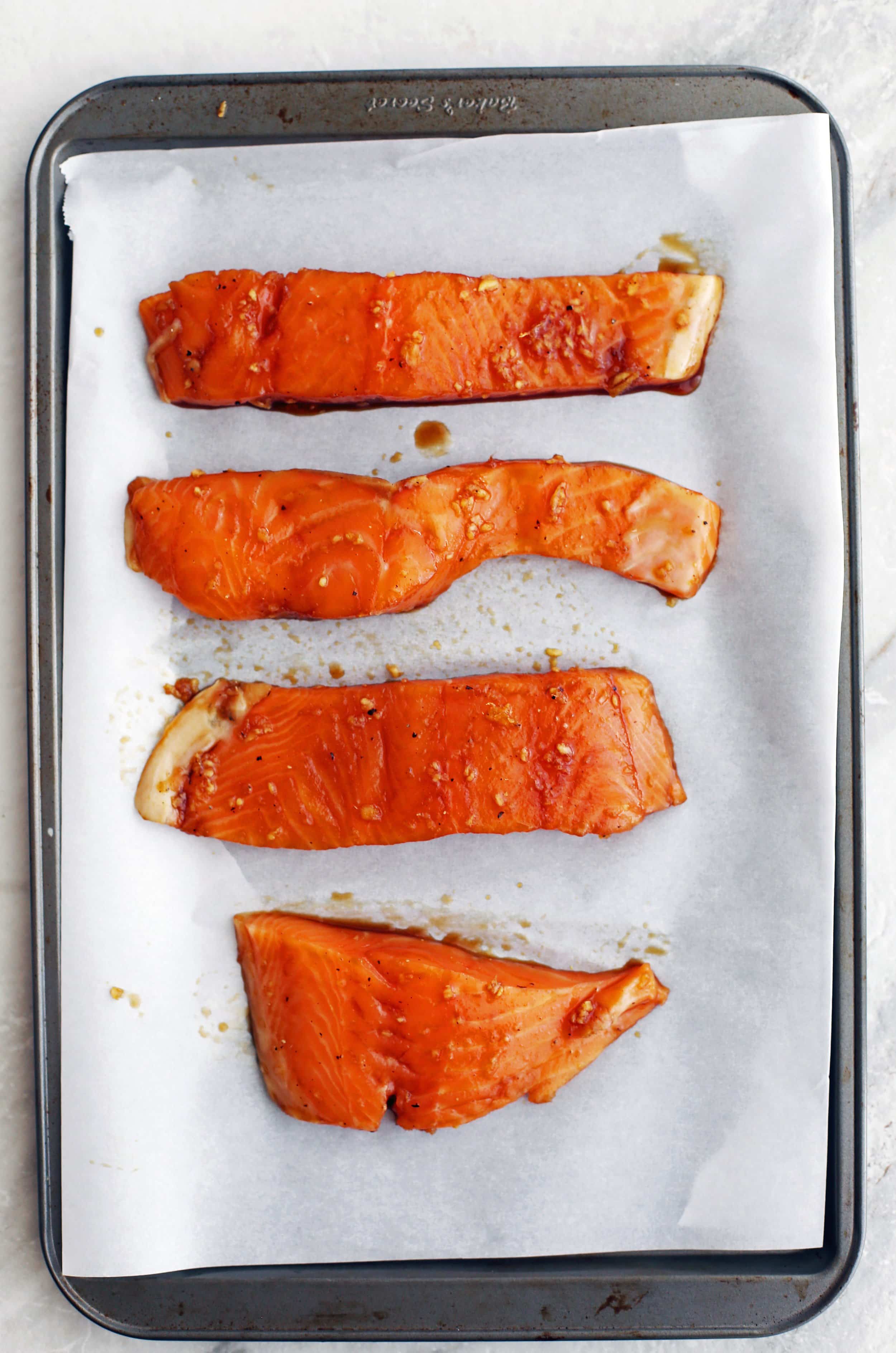 Four maple-soy marinated raw salmon fillets on a baking sheet.